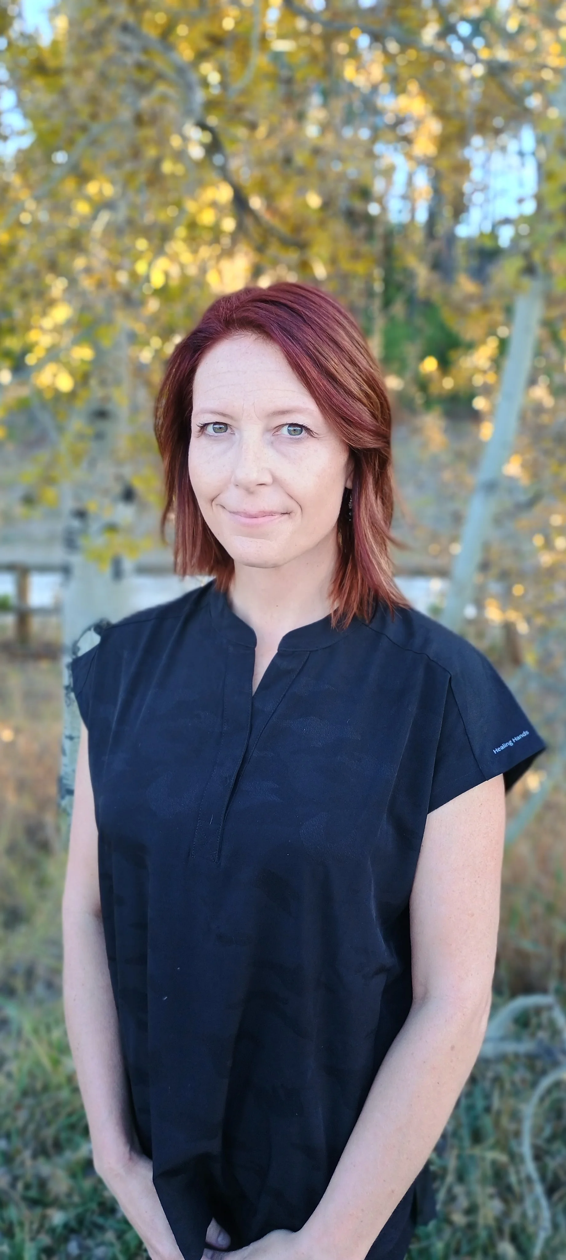 Woman with auburn hair standing in front of fall foliage