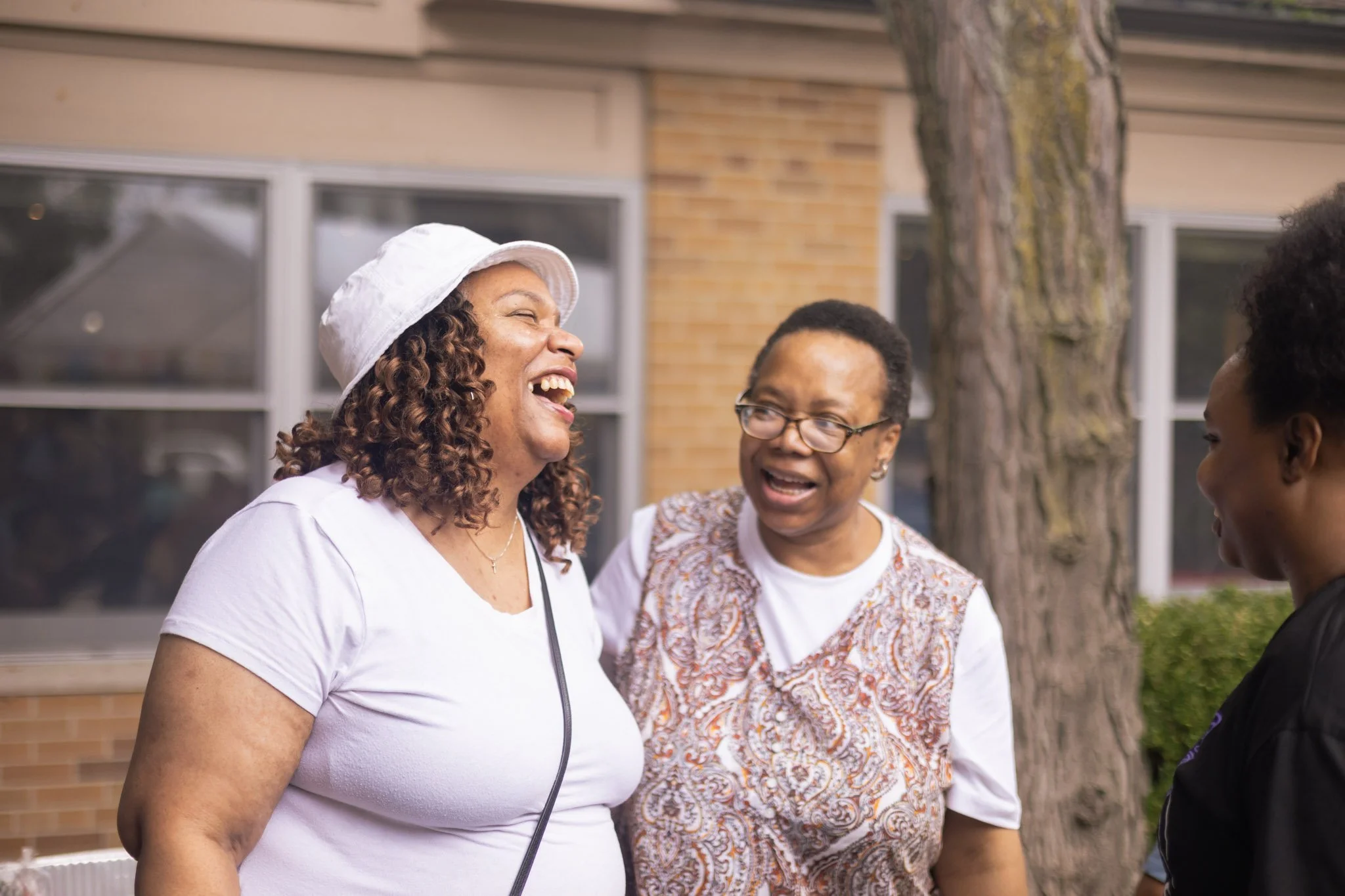 Three people outside, smiling and talking, with one person wearing a white hat.