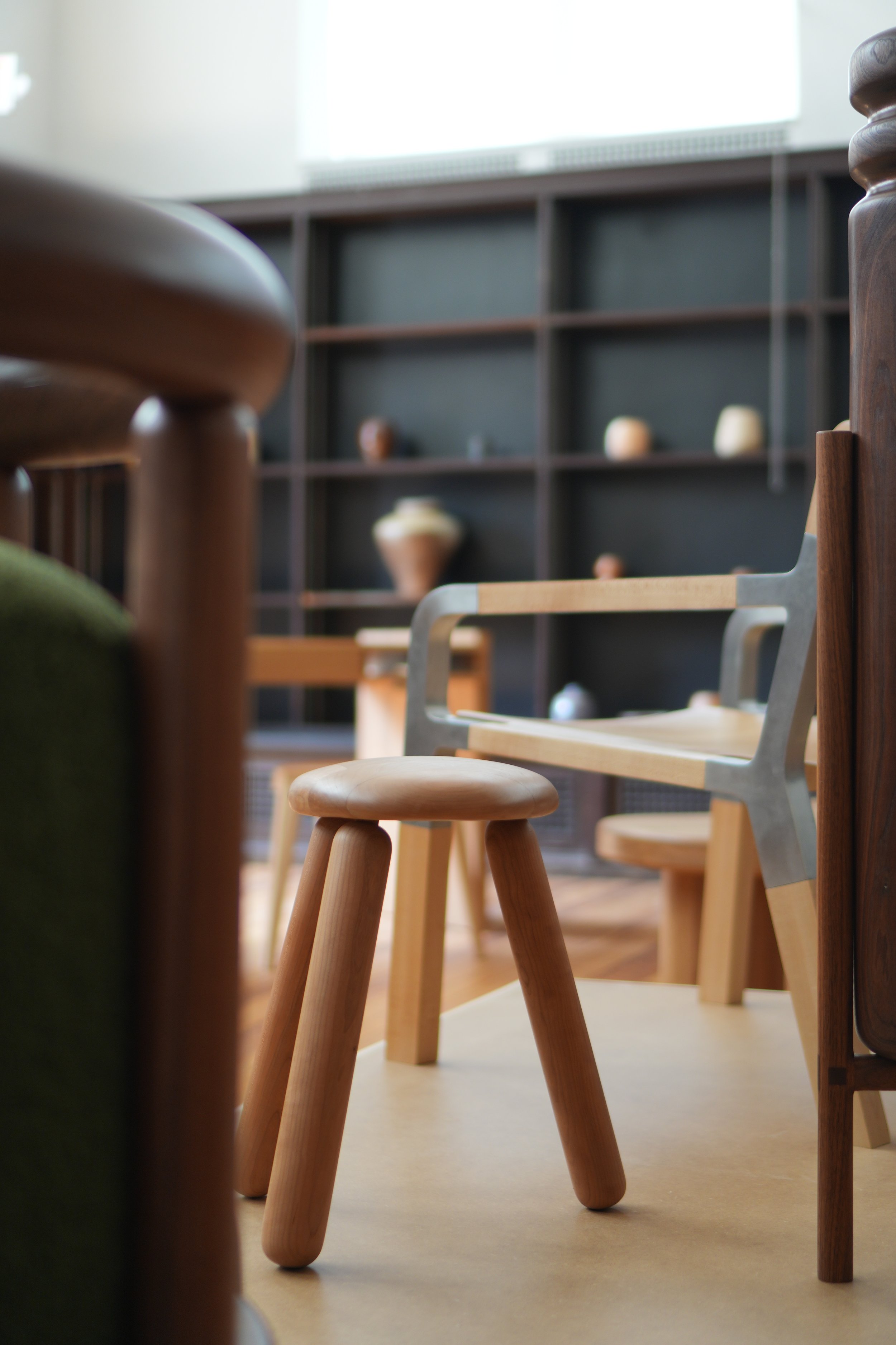 Interior view of a room with wooden chairs and a bookshelf holding decorative objects, with natural light coming through a window.