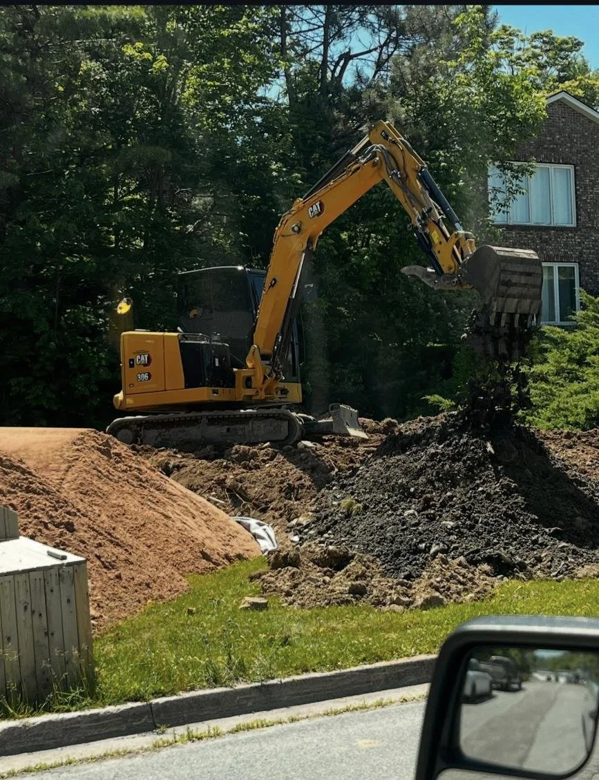 Construction site with a yellow excavator moving dirt piles.