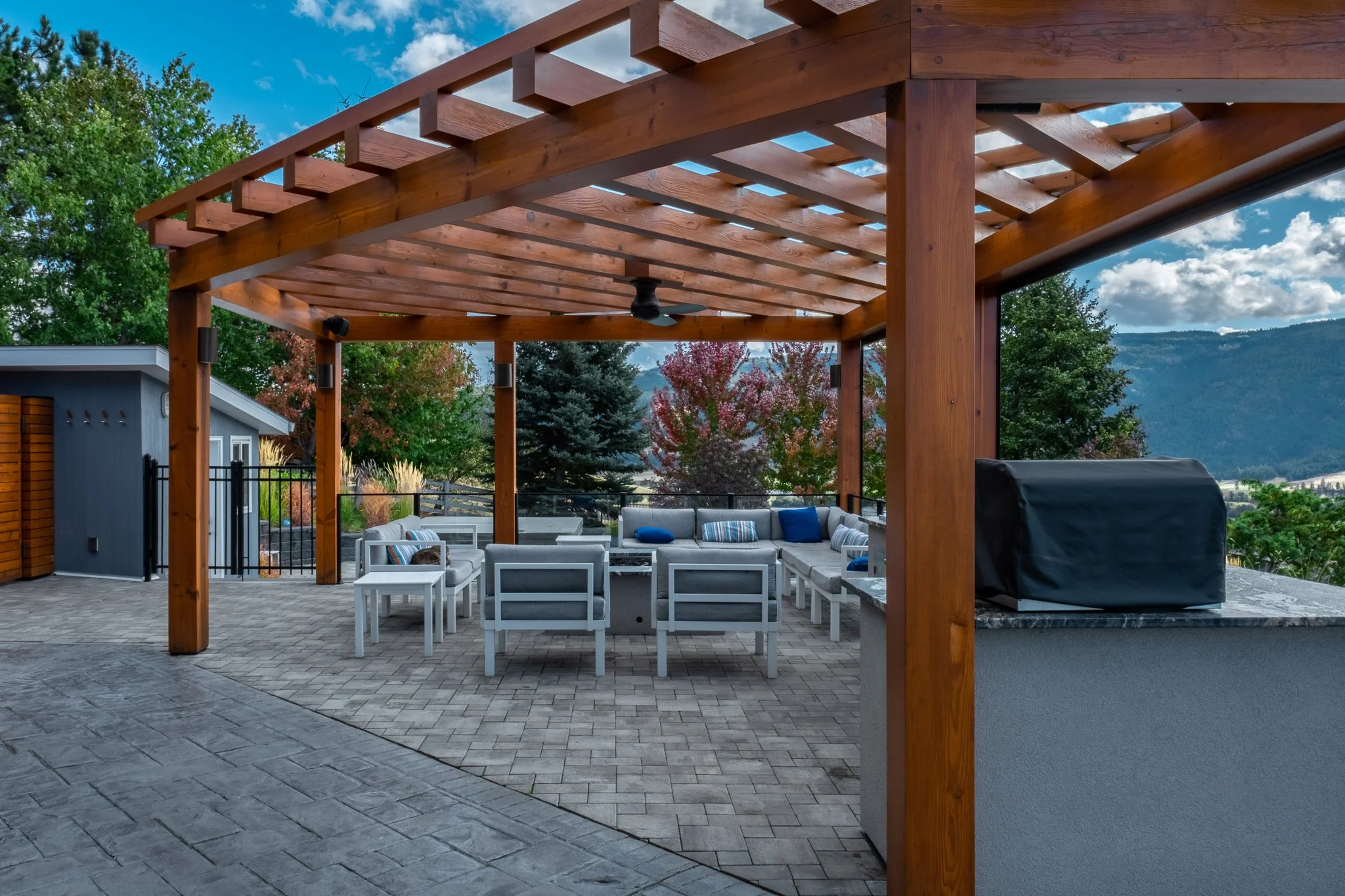 Outdoor patio with wooden pergola, furniture, grill, and scenic view of trees and mountains.