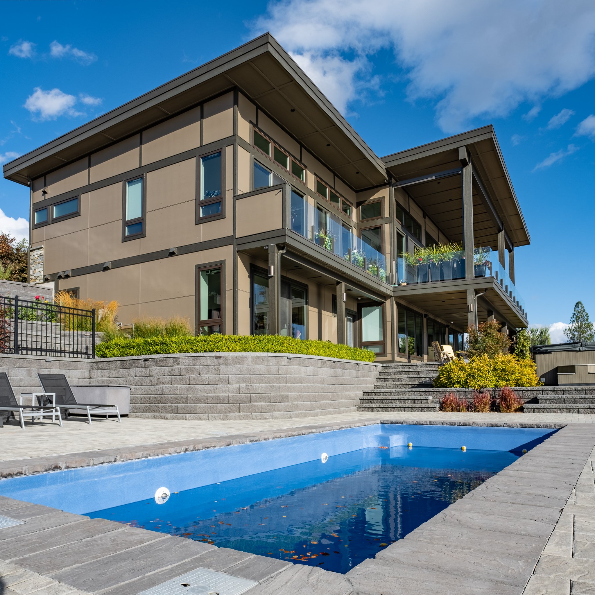 Modern house with a flat roof and large glass windows, exterior view showing concrete steps leading to an empty rectangular swimming pool, surrounded by landscaping and outdoor furniture.