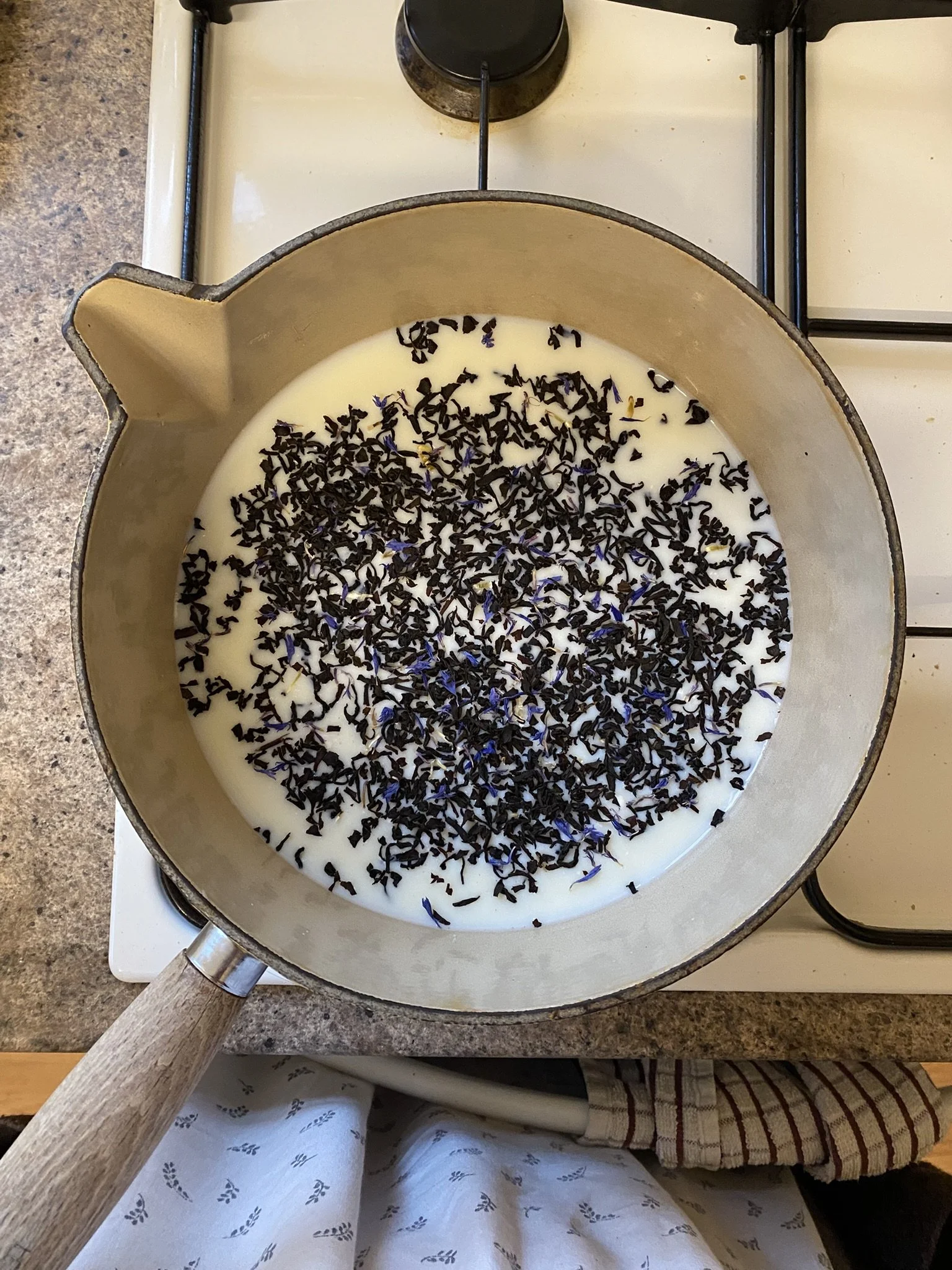 A saucepan on a stove filled with milk and topped with dried lavender blossoms.