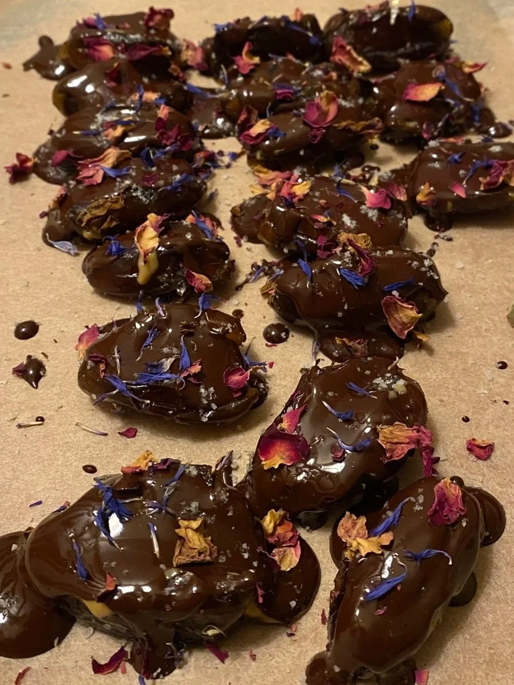 Chocolate-covered candies topped with colorful dried flower petals on a brown paper surface.