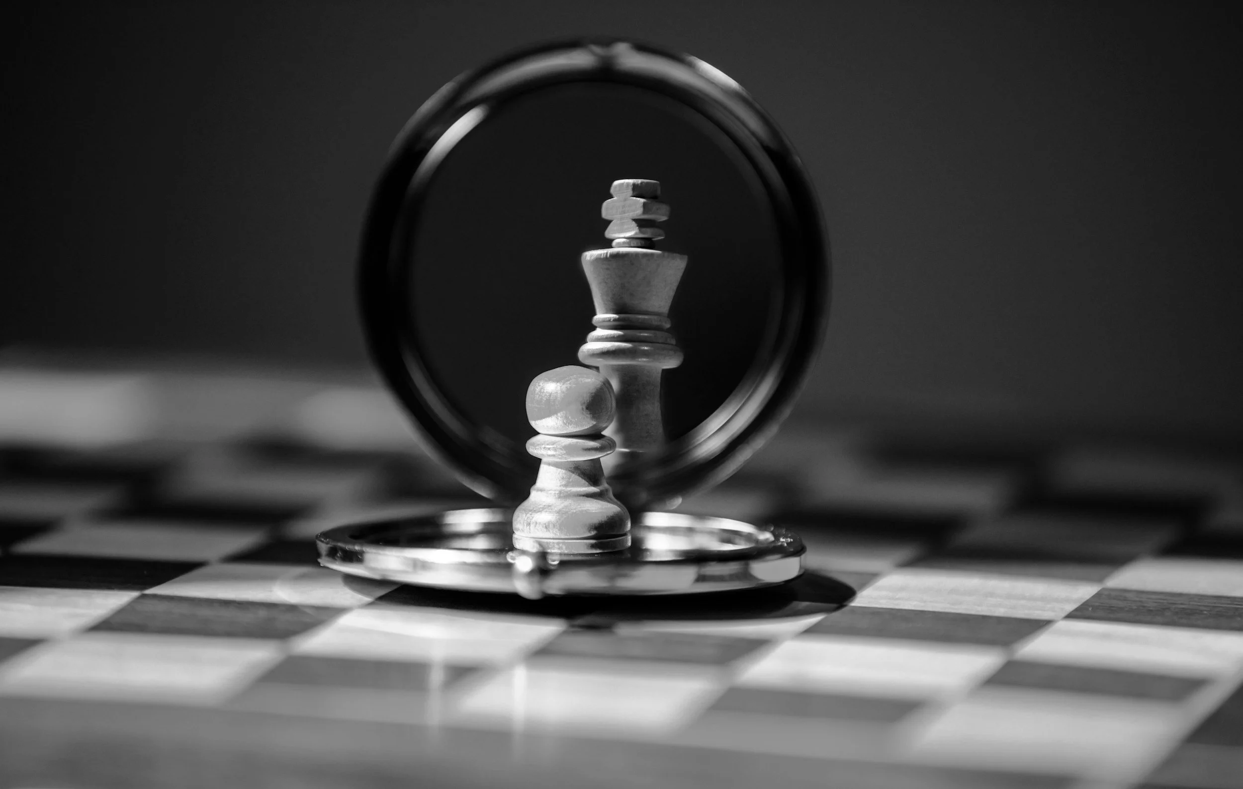 A black-and-white chessboard with a pawn in front of a mirror reflecting a queen chess piece.
