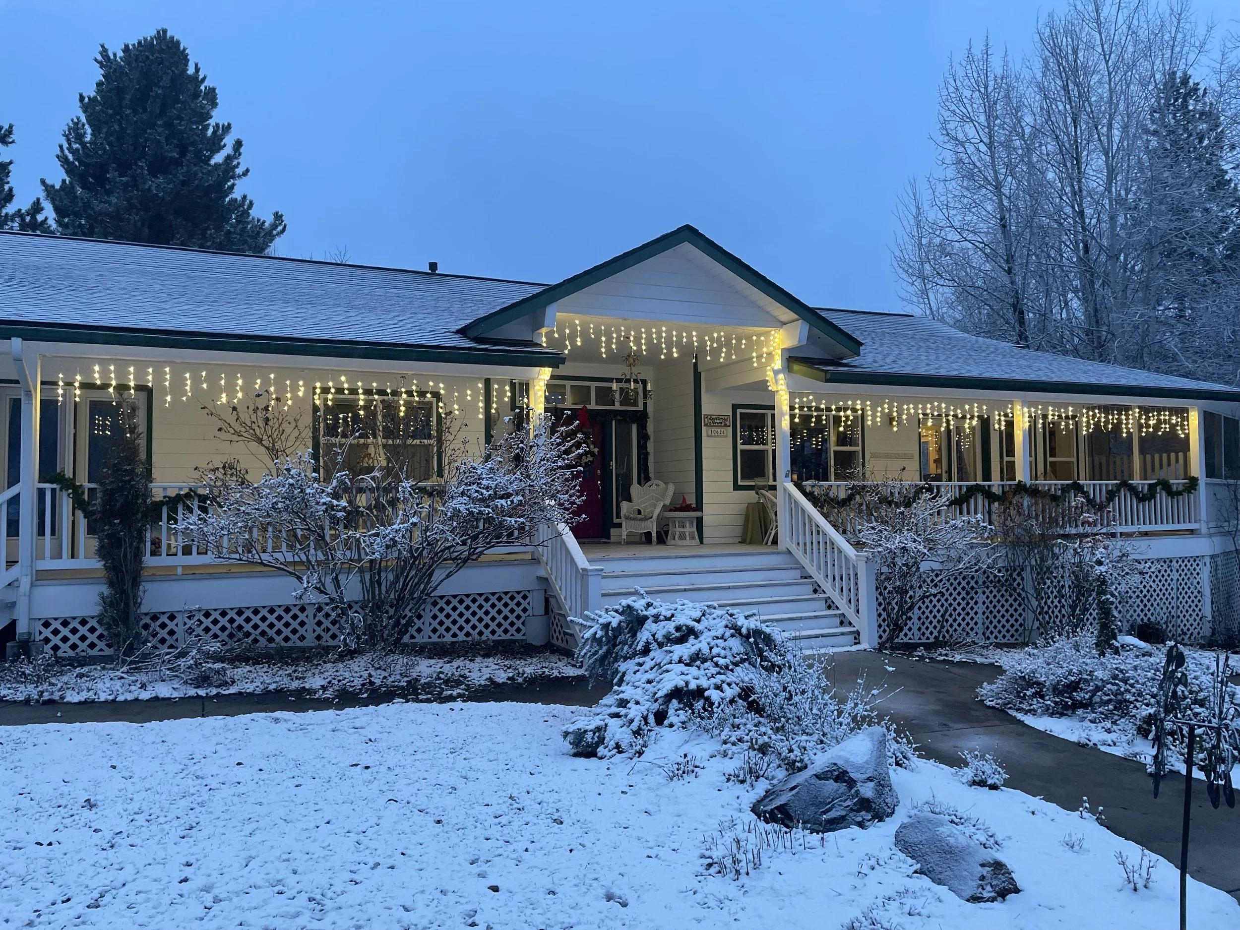 Snow-covered house with icicle Christmas lights and a front porch in a winter setting.