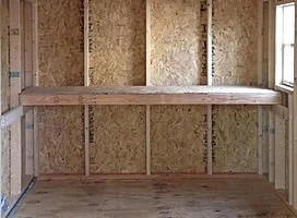 Interior of a partially constructed wooden shed with visible framing and a shelf.