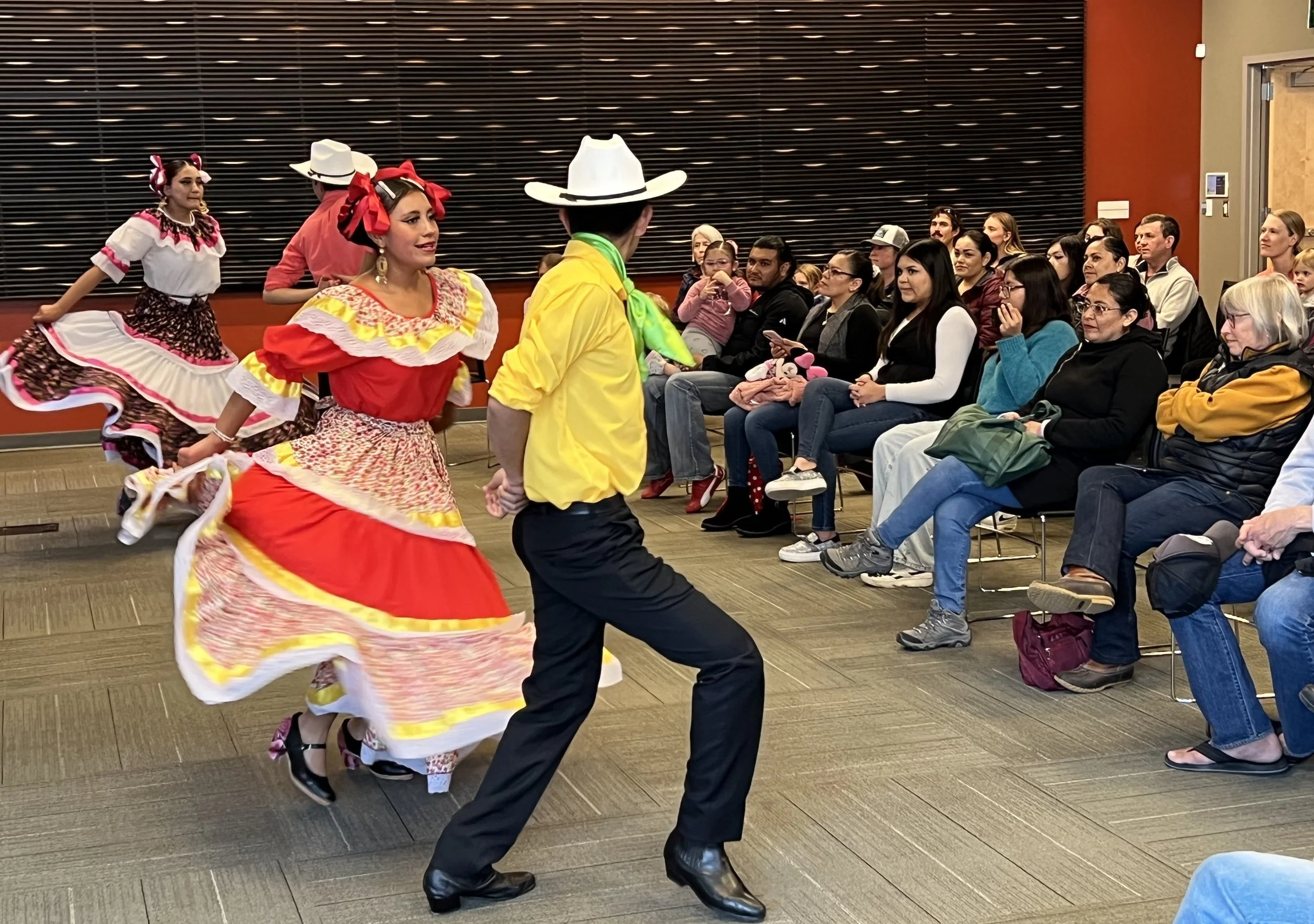 Mexican dancers performing folkloric dance in front of seated audience.