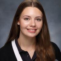 Young woman with long brown hair, wearing a black shirt with white accents, smiling at the camera.