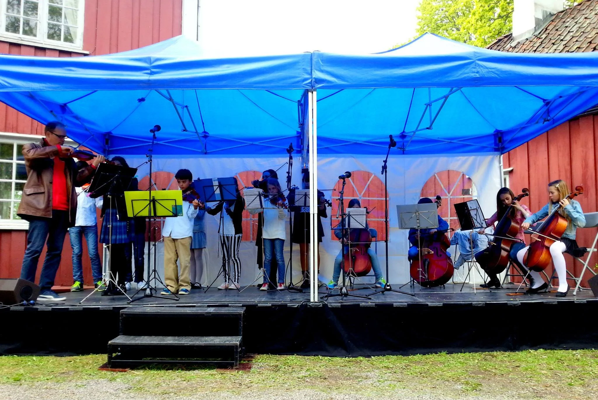 Gruppe unge musikere som spiller strykeinstrumenter under et blått telt.