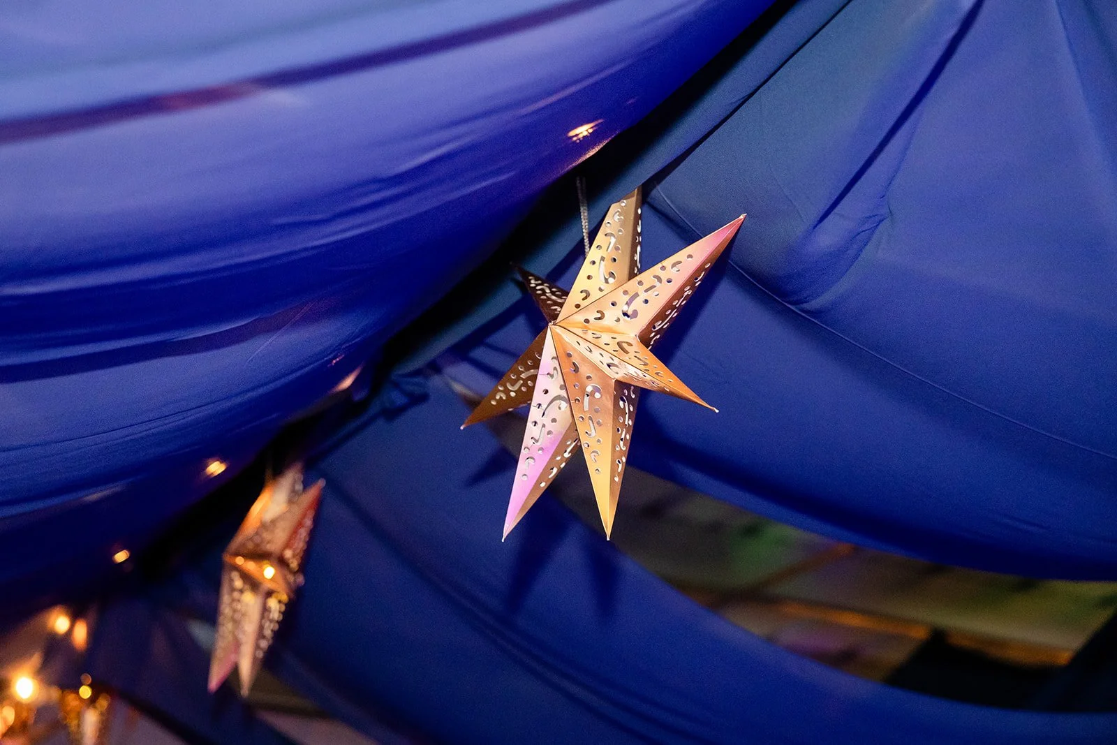 Decorative gold star-shaped lanterns hanging against a blue fabric background.