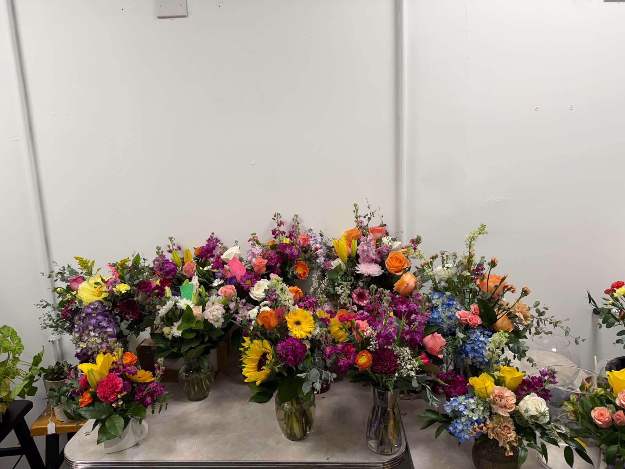 Various colorful flower arrangements in vases against a plain wall.