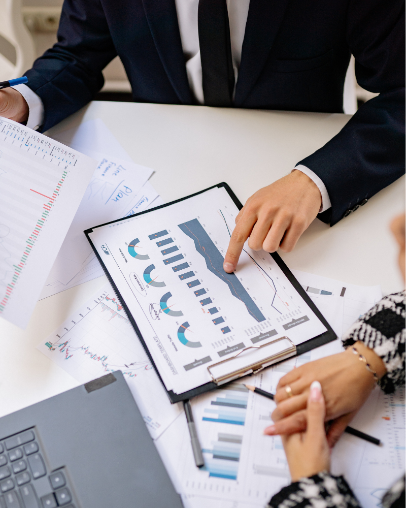 Imagen de reunión de negocios con dos personas analizando gráficos y datos en una mesa de oficina.