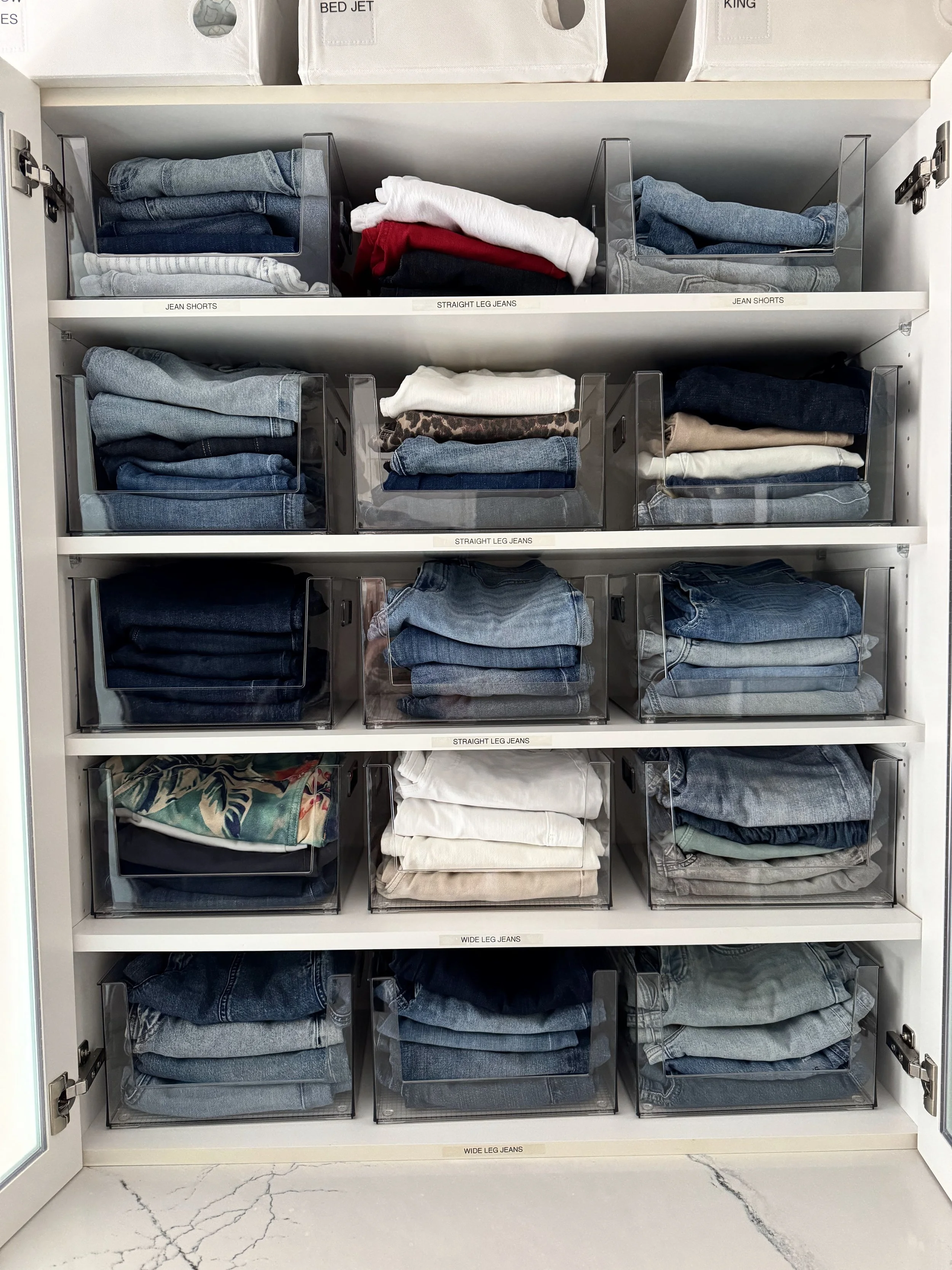 White cabinet with folded jeans and pants organized on shelves