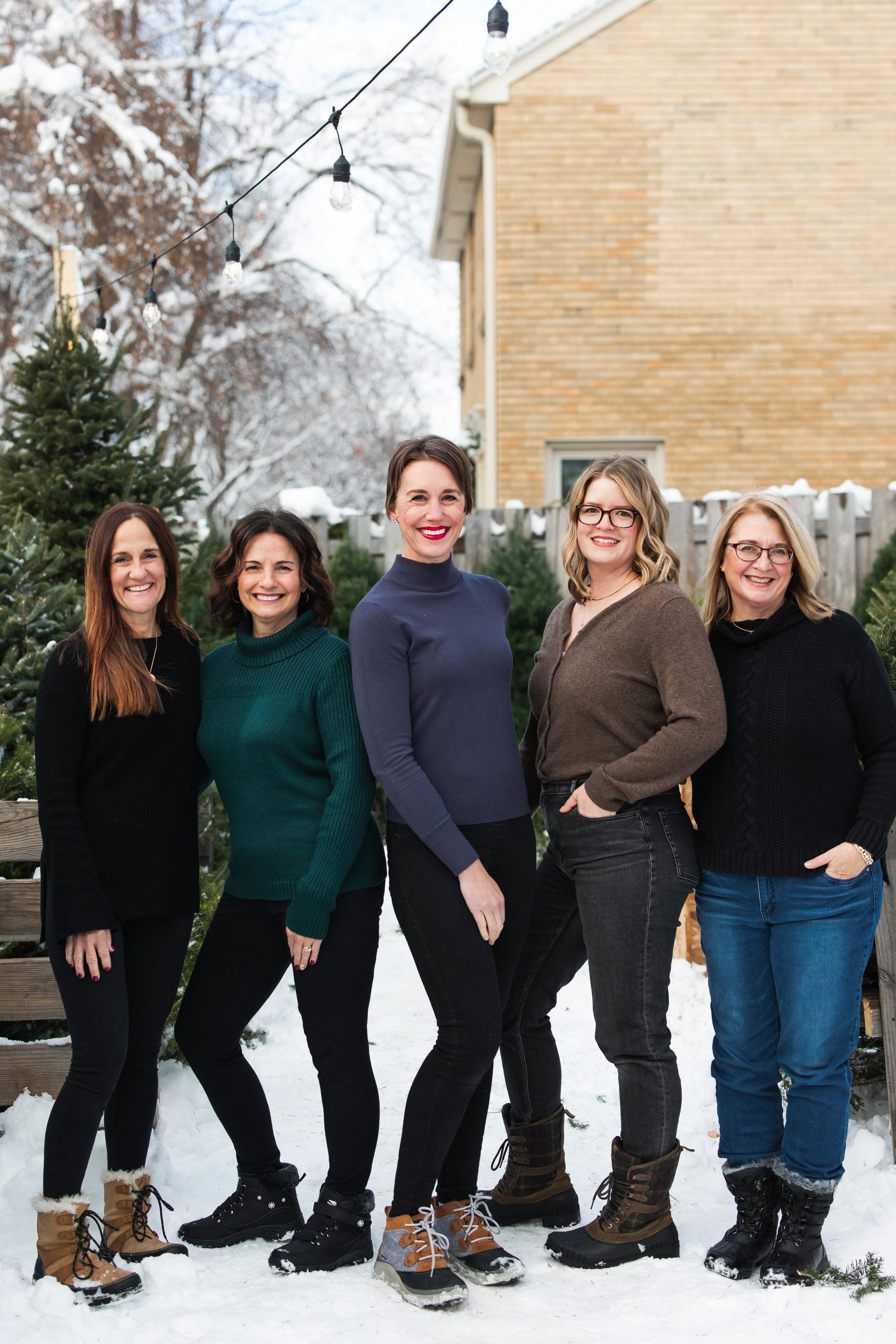 Five women in sweaters and jeans standing outside and smiling