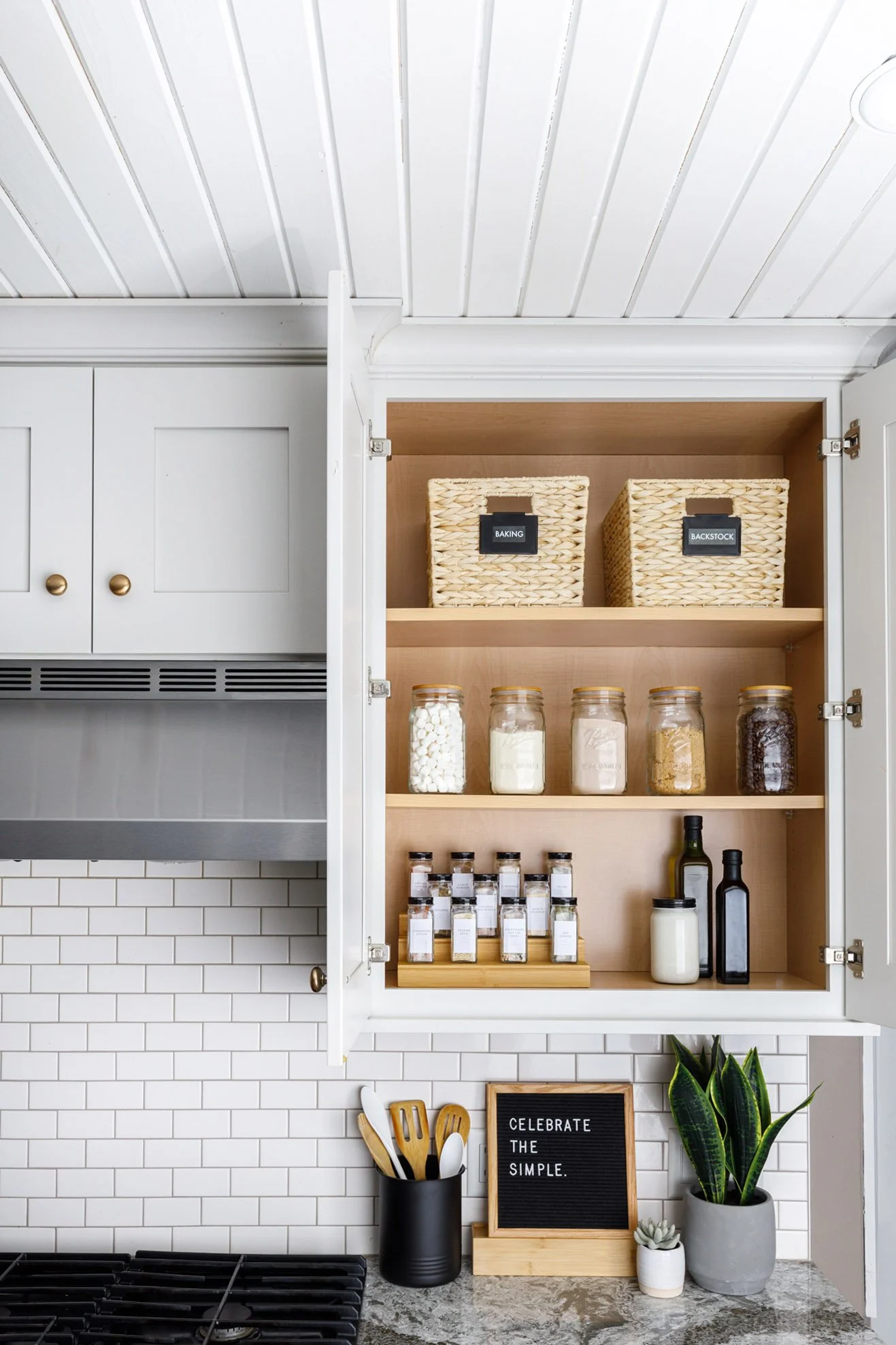 a white cabinet with pretty spices and clear jars, and a sign saying 'celebrate the simple'