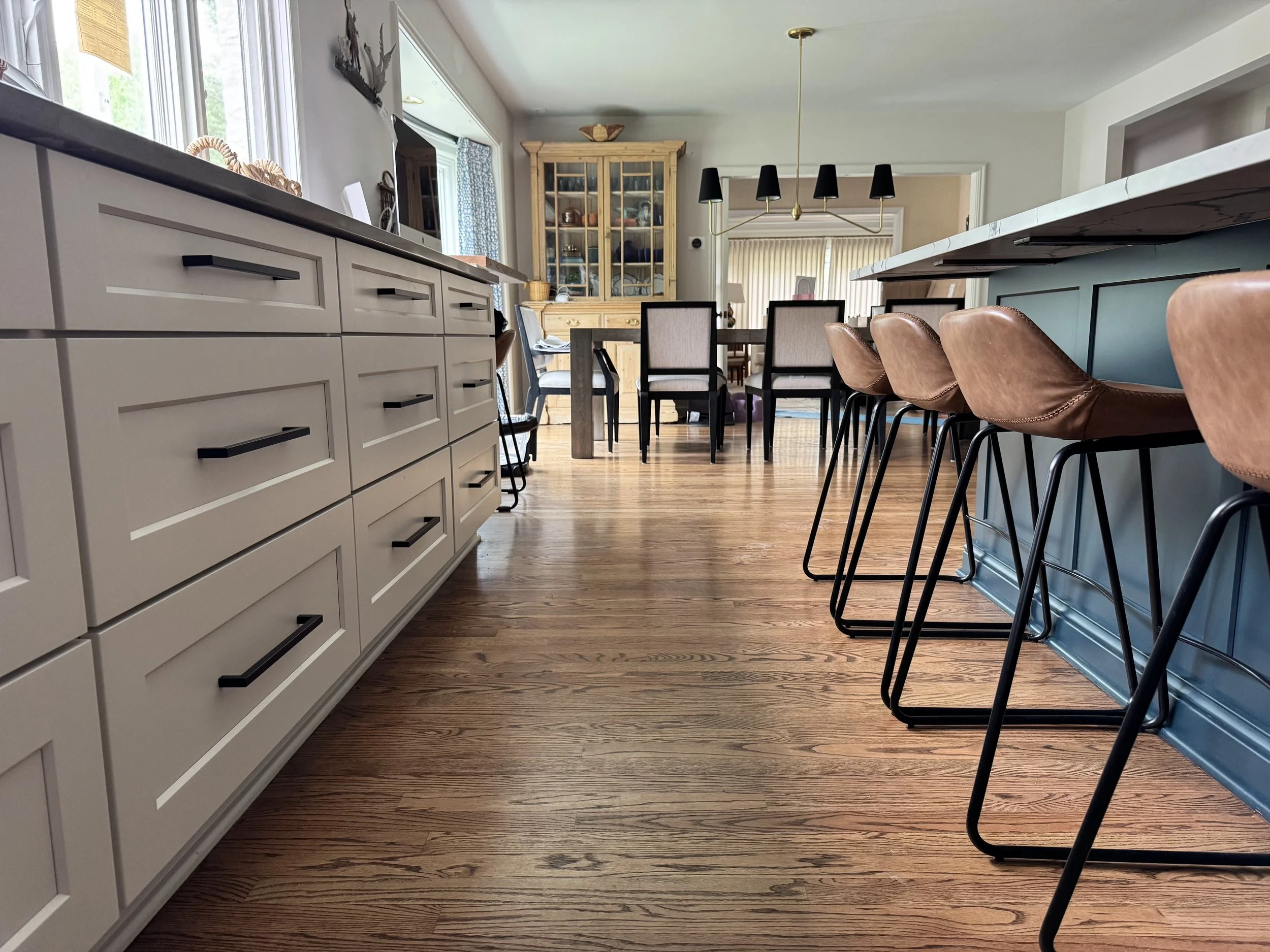 kitchen cabinets that are white with brown leather chairs at an island