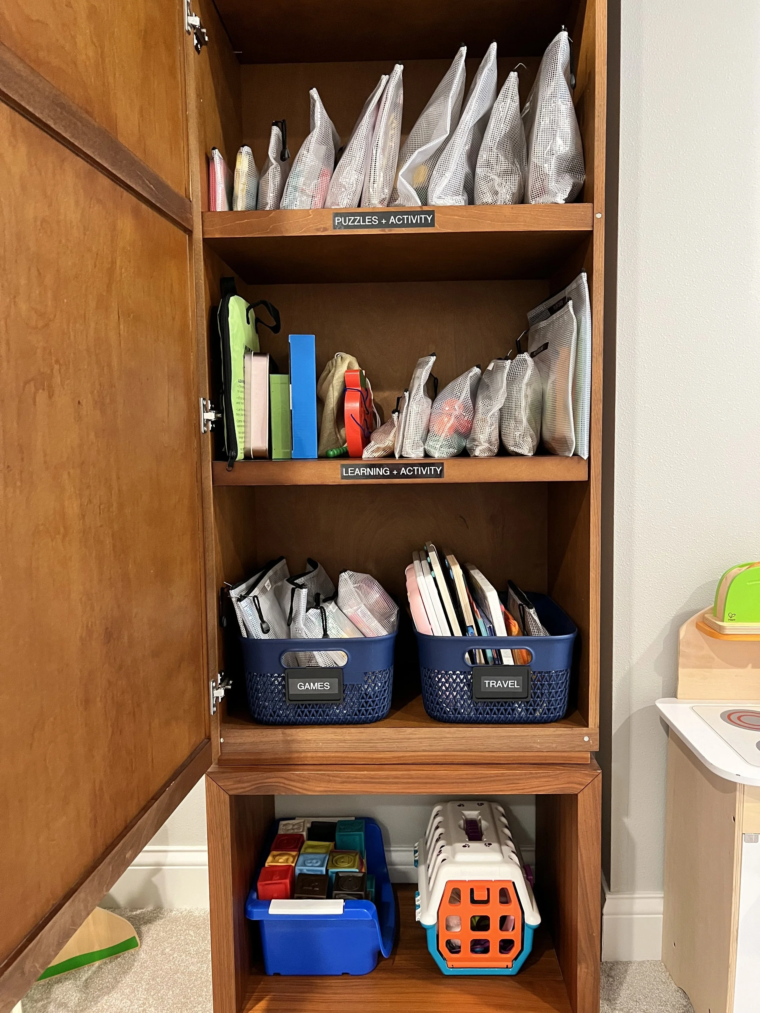 A wooden cabinet with zipper bags organizing games for kids' play space
