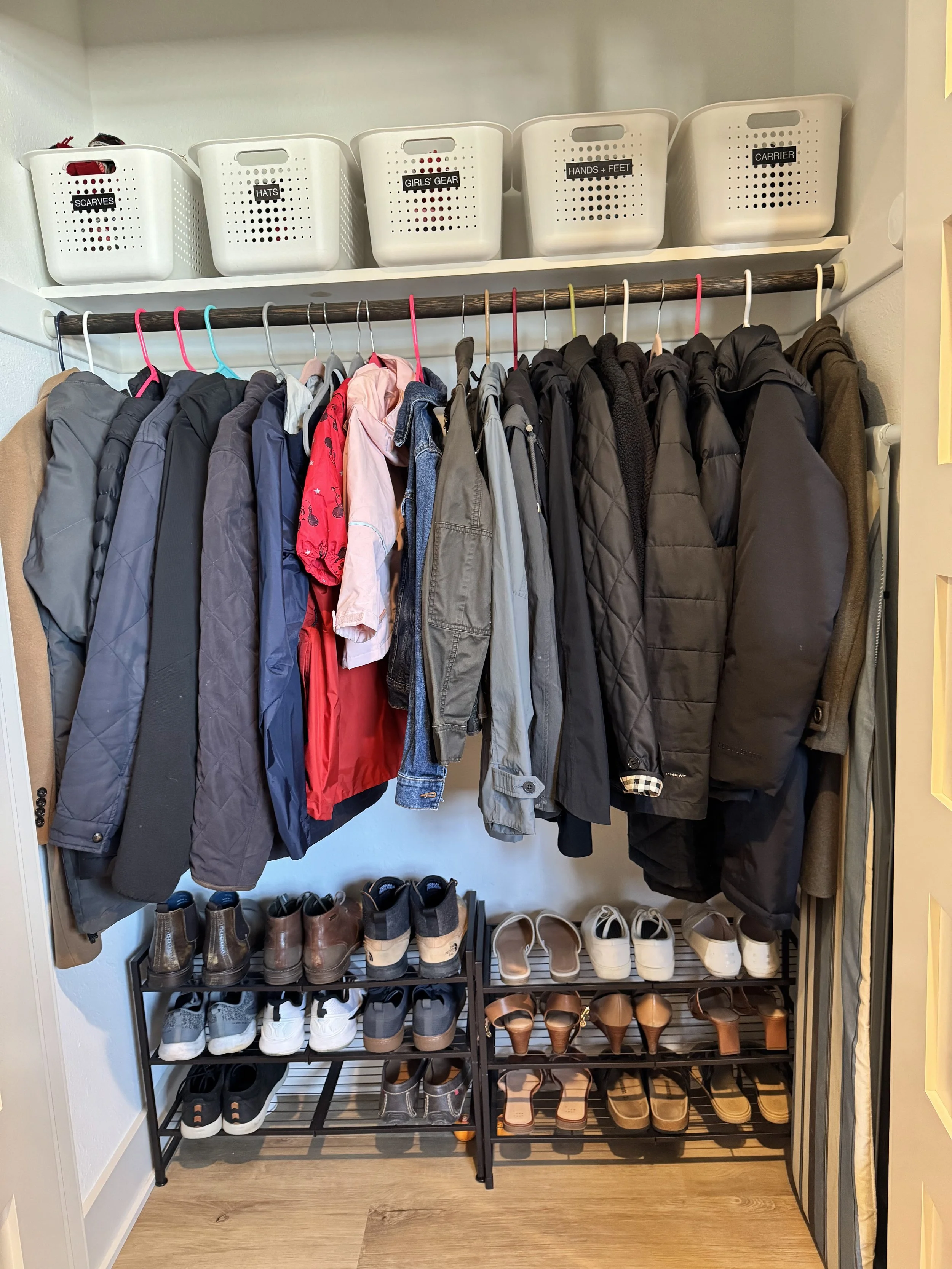 Coats hanging with a shoe rack and organized bins on the top shelf
