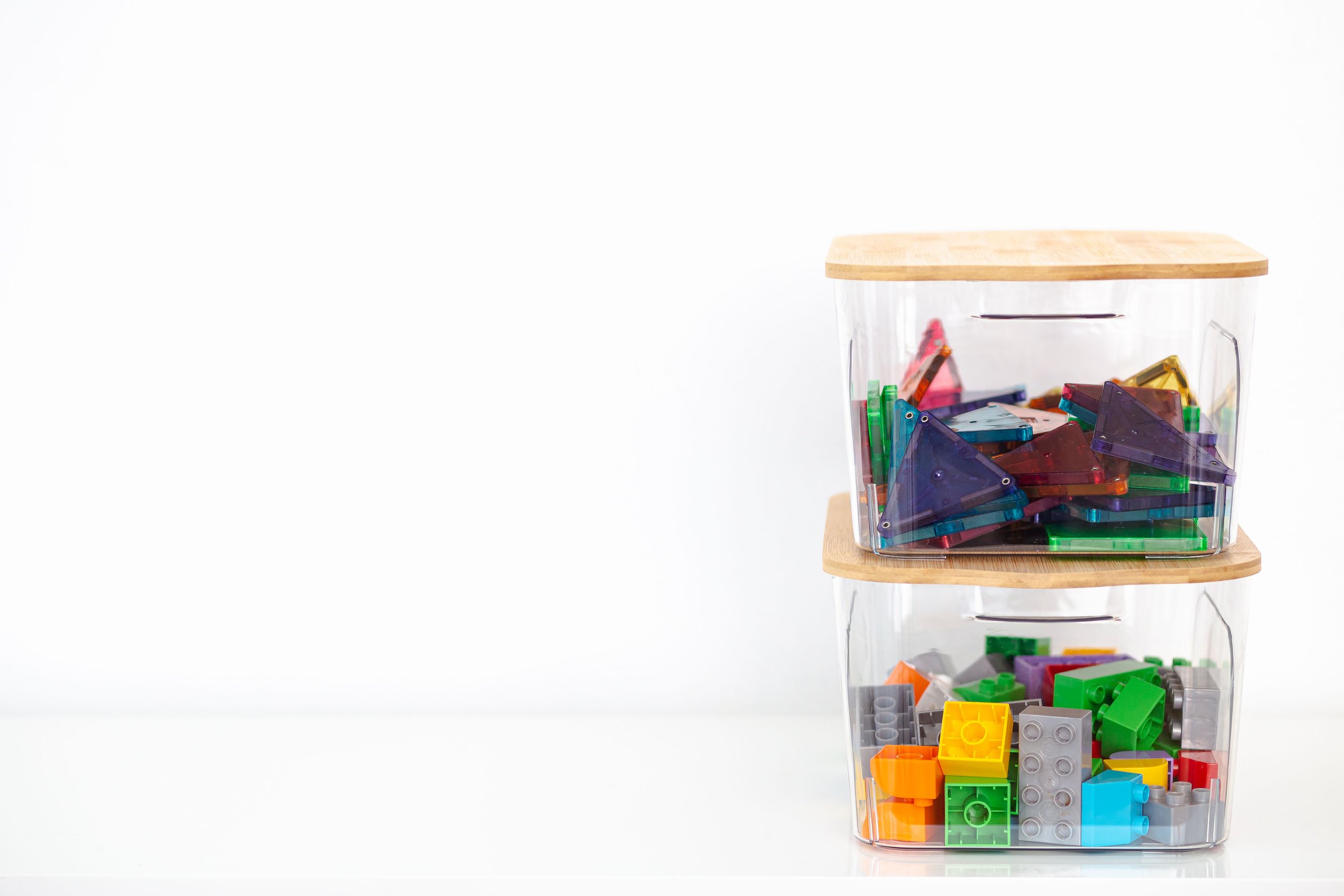 clear bins with wooden lids and bright colored toys inside