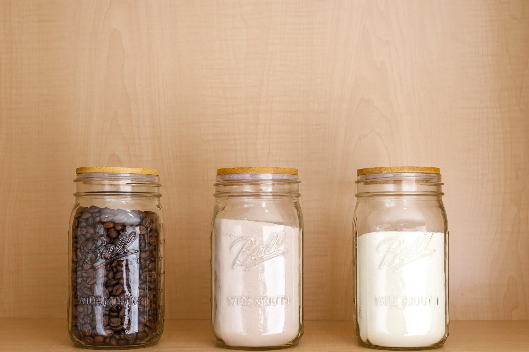 Three clear jars with wooden lids holding coffee beans and flours