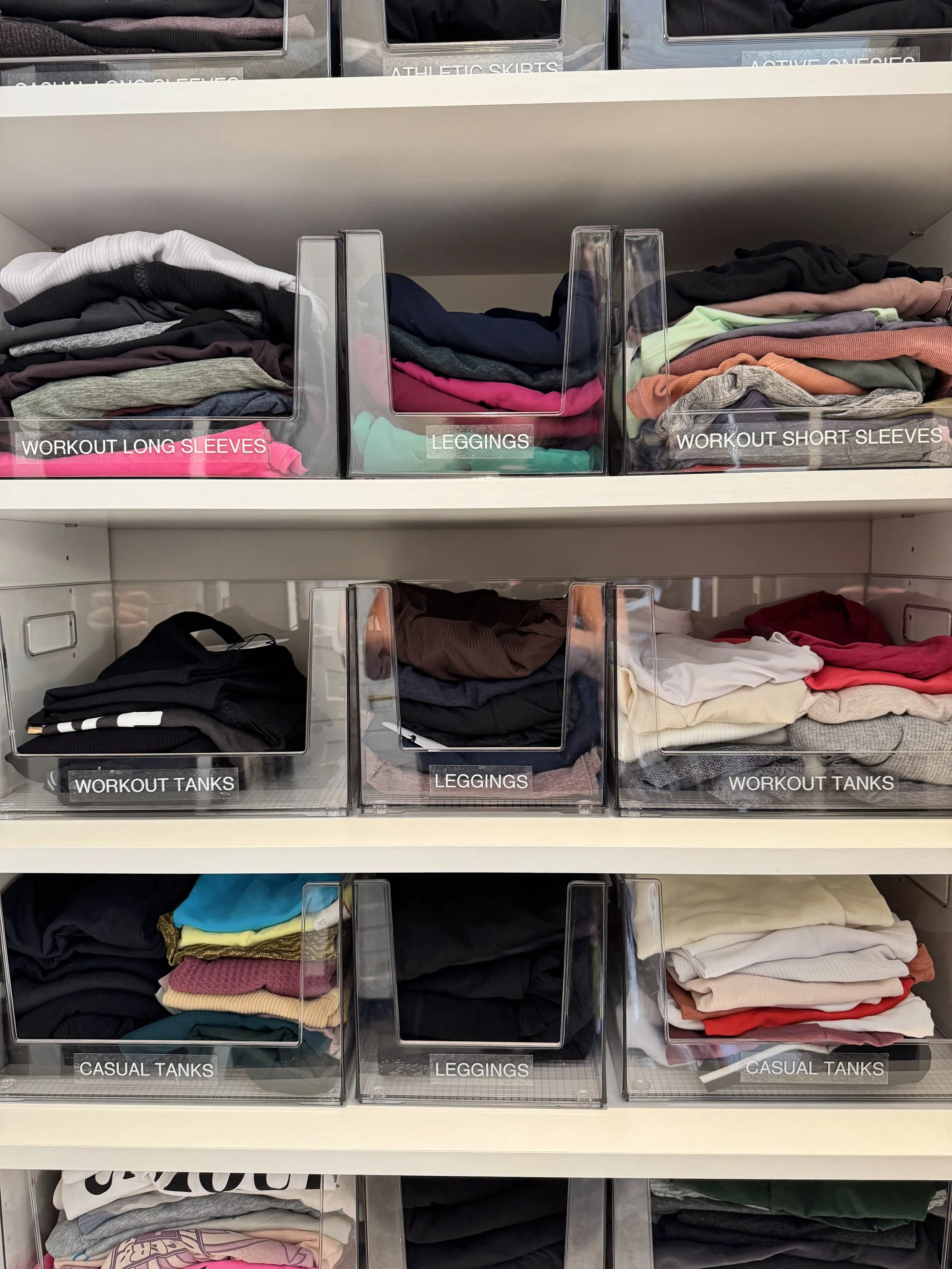 White cabinet with folded athletic clothing in clear bins with labels, organized on shelving