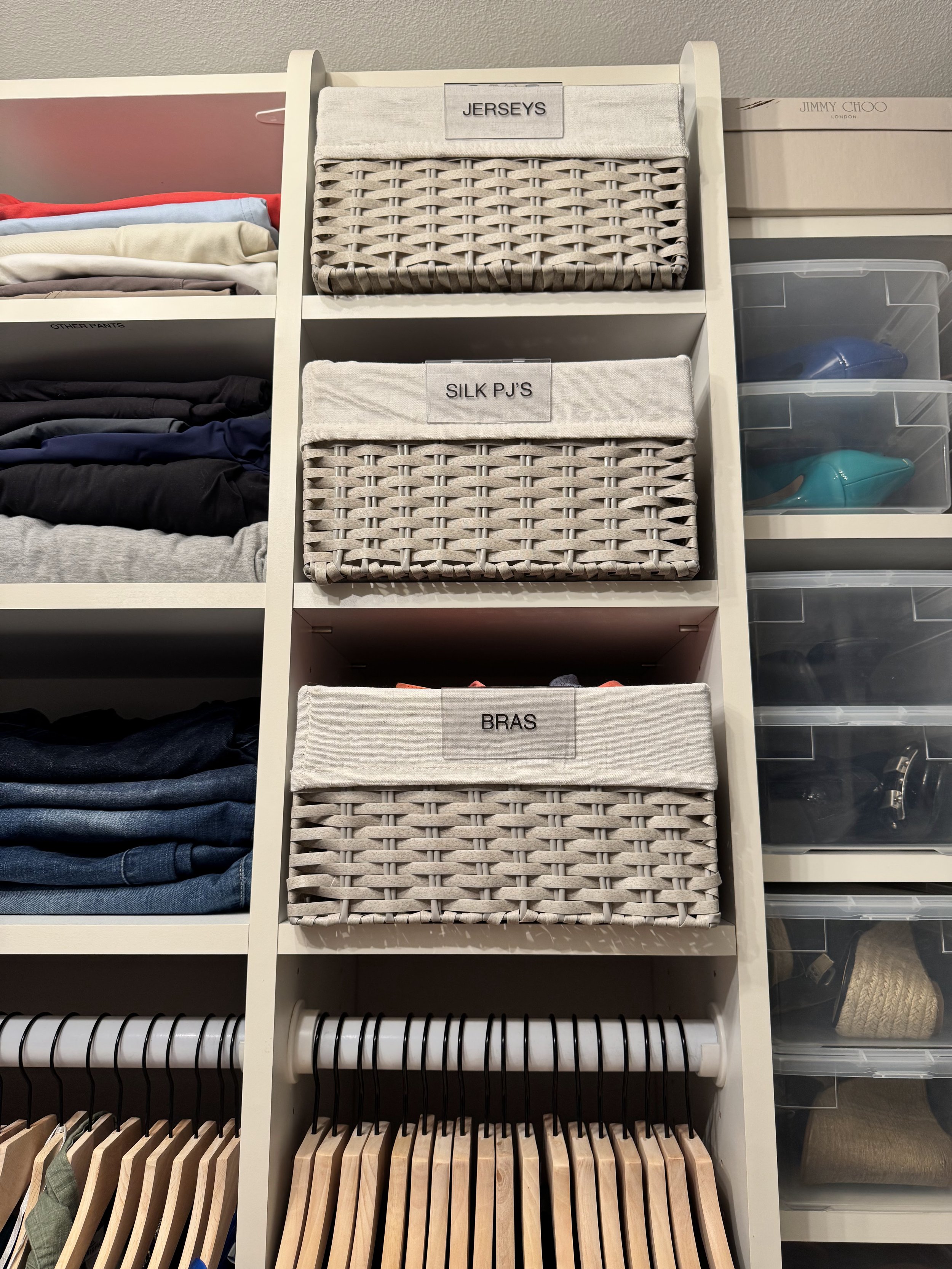 Woven gray baskets inside of a closet with wooden hangers and folded clothing