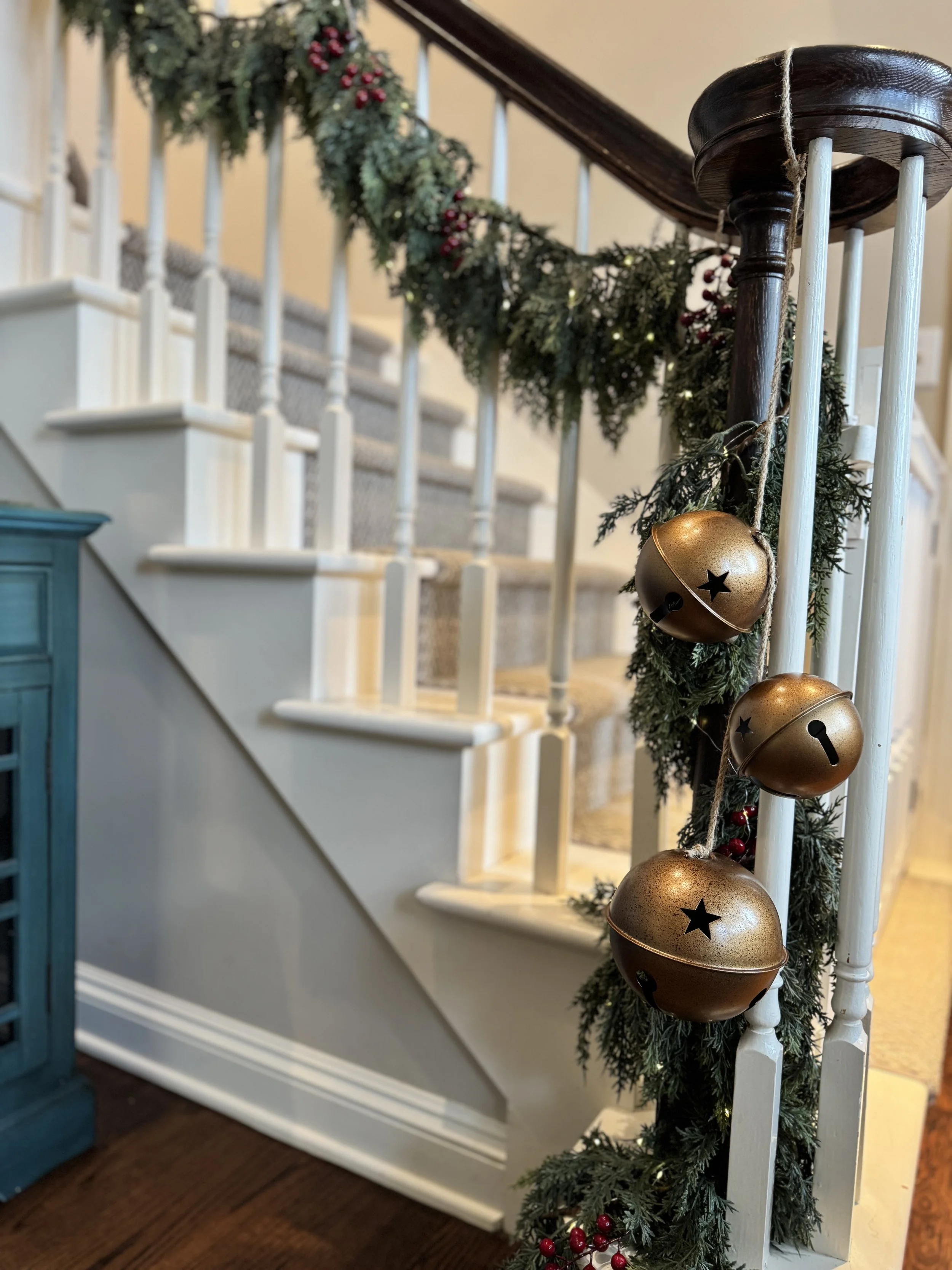 Gold bells and cedar garland hanging on a stairway banister with lights and cranberries