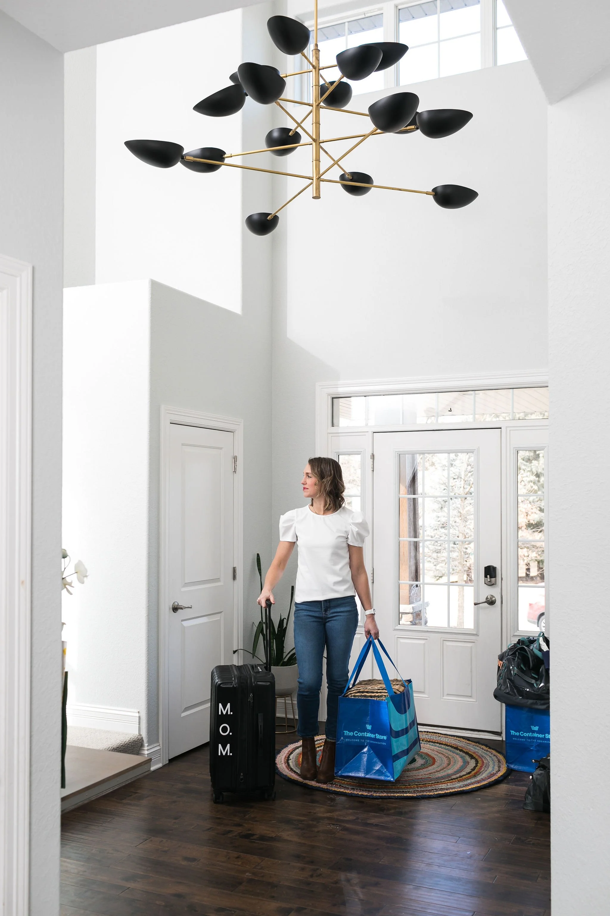 woman in a white top and blue jeans pulling a black suitcase in a home entry