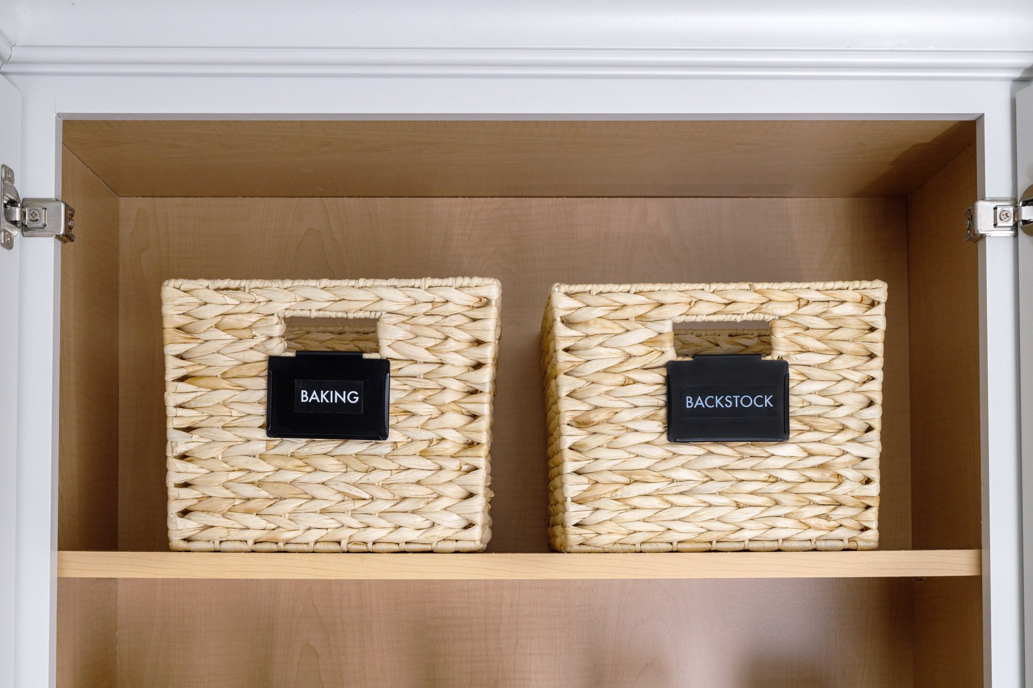 two pretty woven baskets with lack labels in a white cabinet