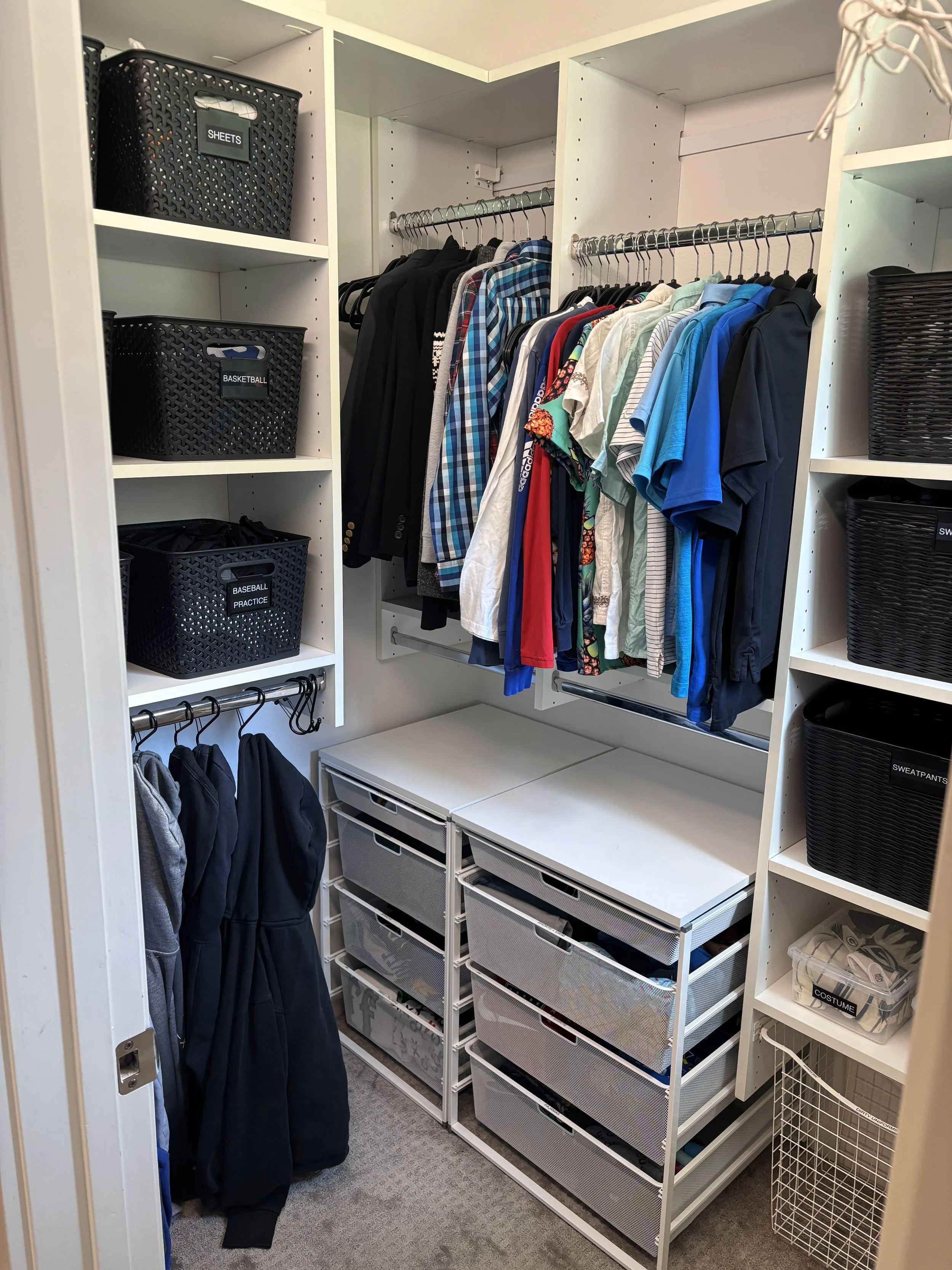 Black baskets with labels, hanging clothing, and metal drawers in a kids' closet