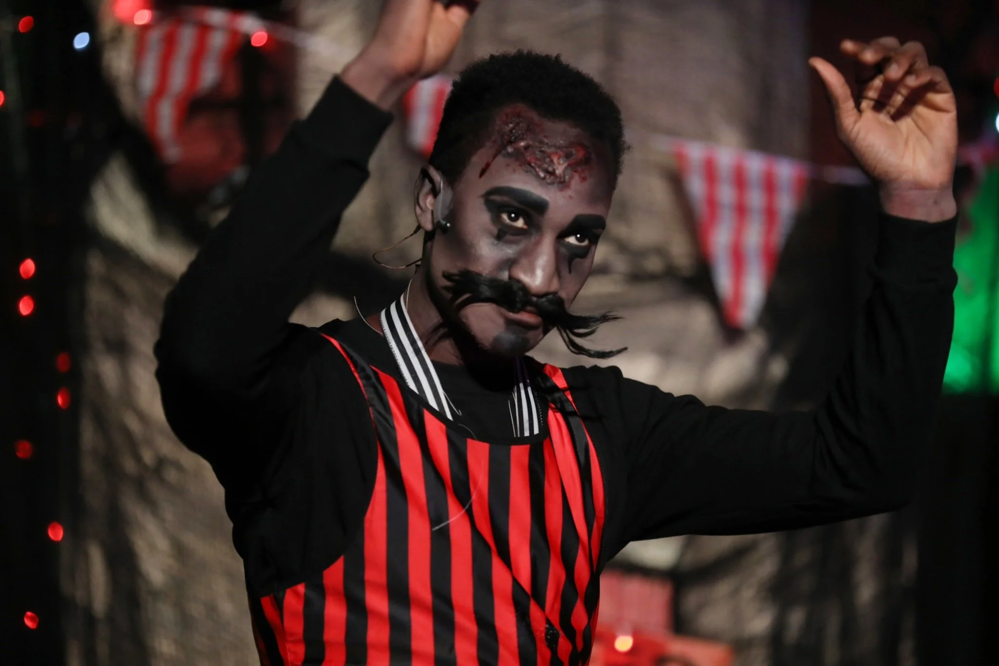 Person in theatrical Halloween costume with striped outfit and dramatic face makeup.