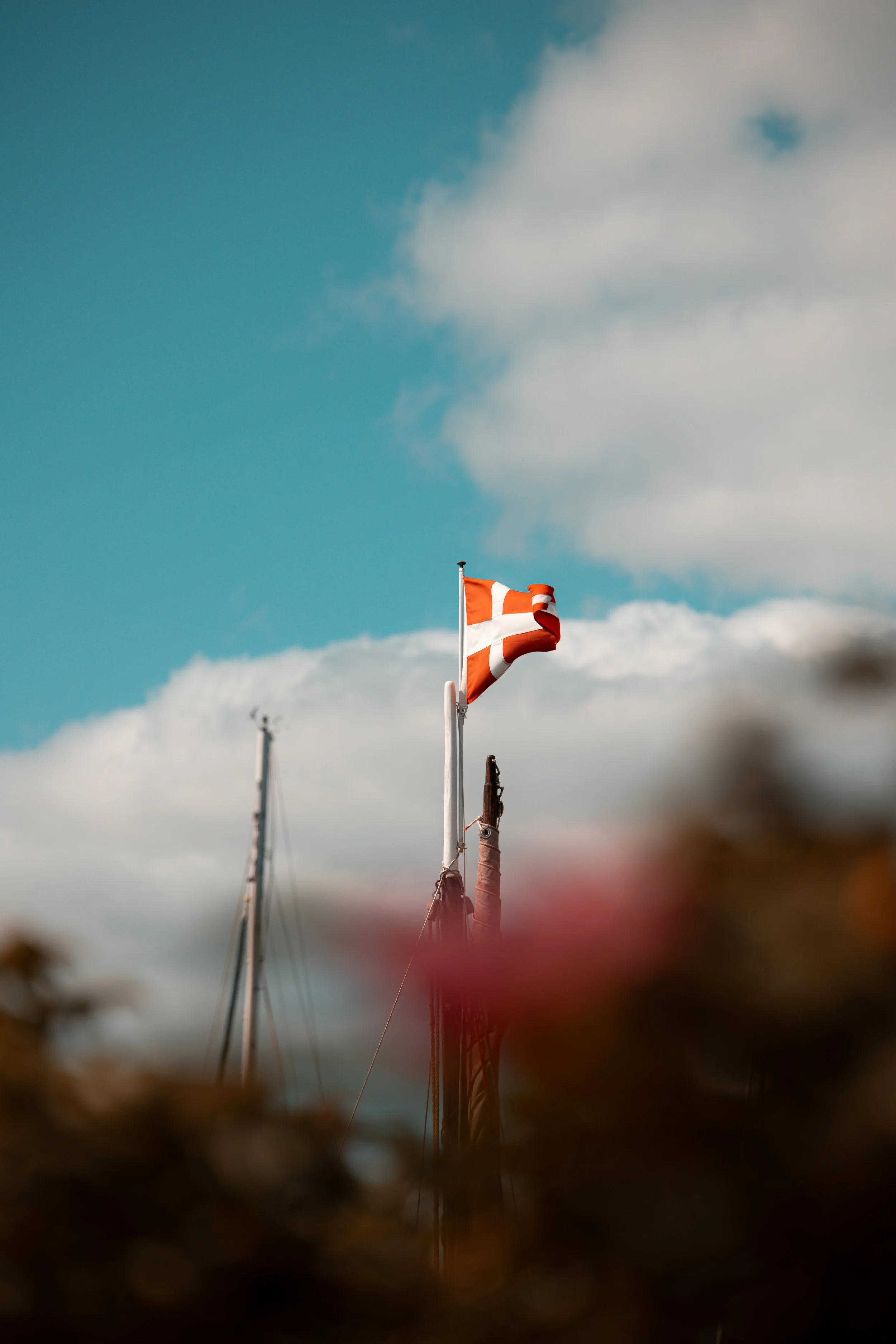 A Danish flag flying on a boat's mast against a partly cloudy sky.