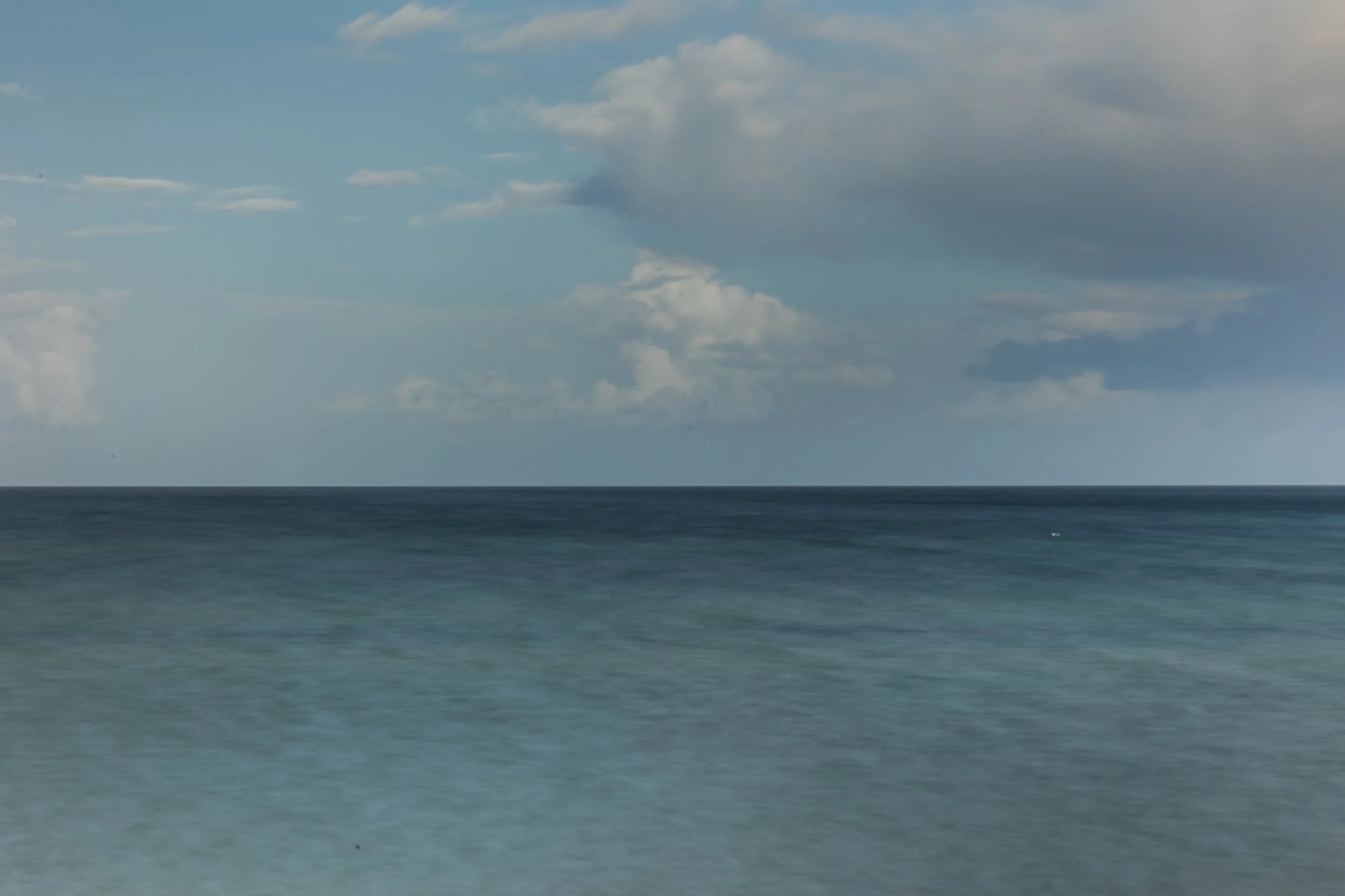 Calm ocean with blue sky and scattered clouds.
