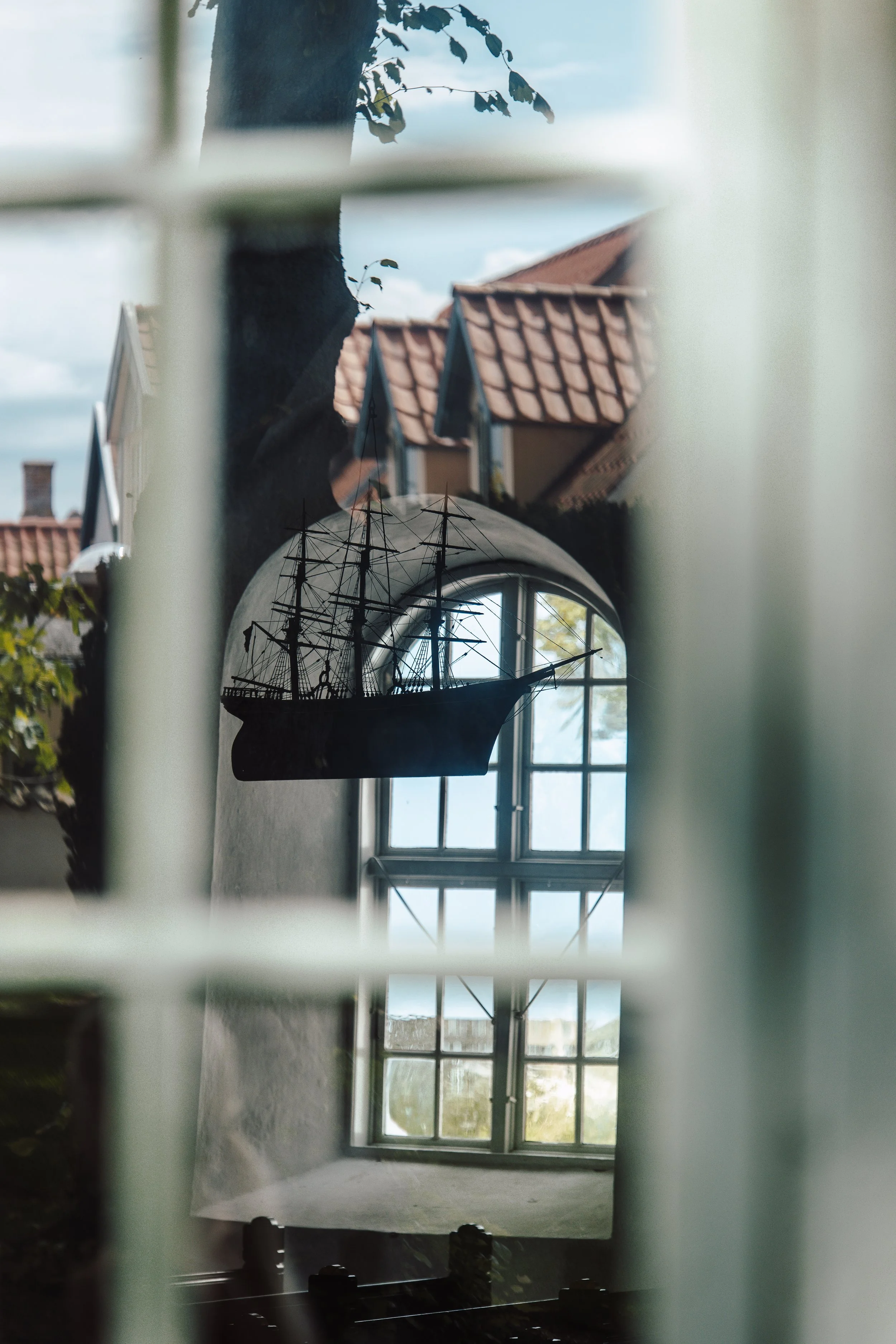A reflection of a ship model seen through a window and then through a mirror, with a house roof visible in the background.