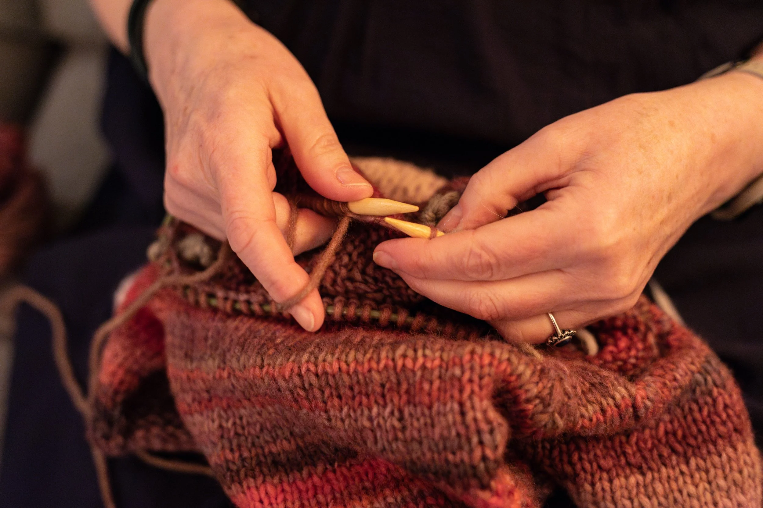 Close-up of hands knitting with wooden needles and multicolored yarn. This is a perfect indoor activity for tourists traveling the the Faroe Islands during autumn and winter.