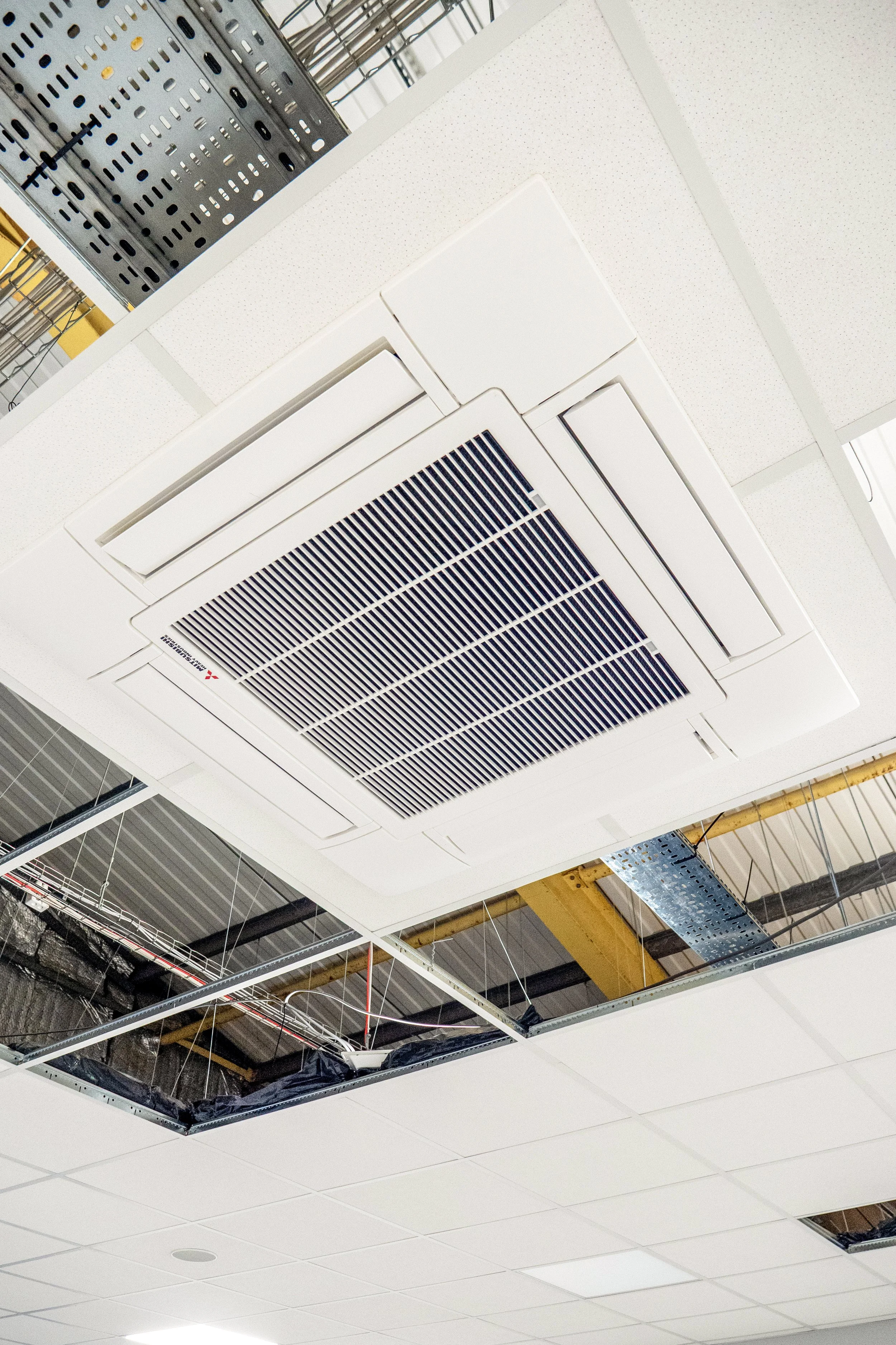 Ceiling with open panels, exposed ducts and pipes, part of an industrial or commercial building under construction or renovation.