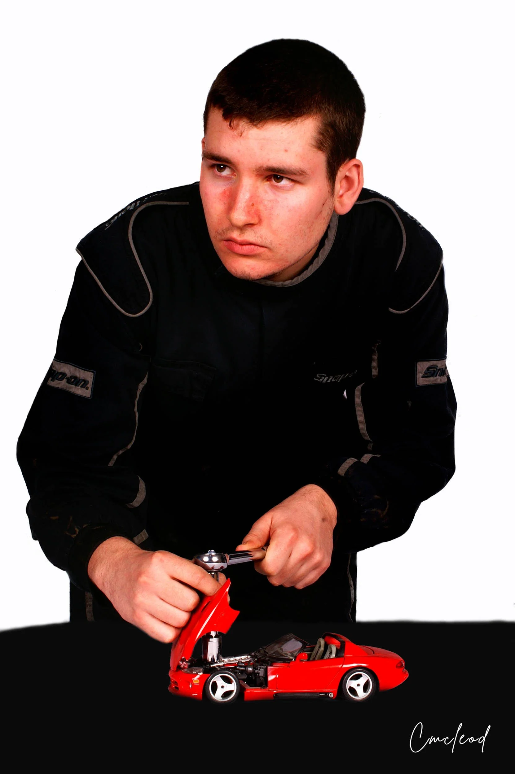Man in racing suit working on a red toy race car with a black background.