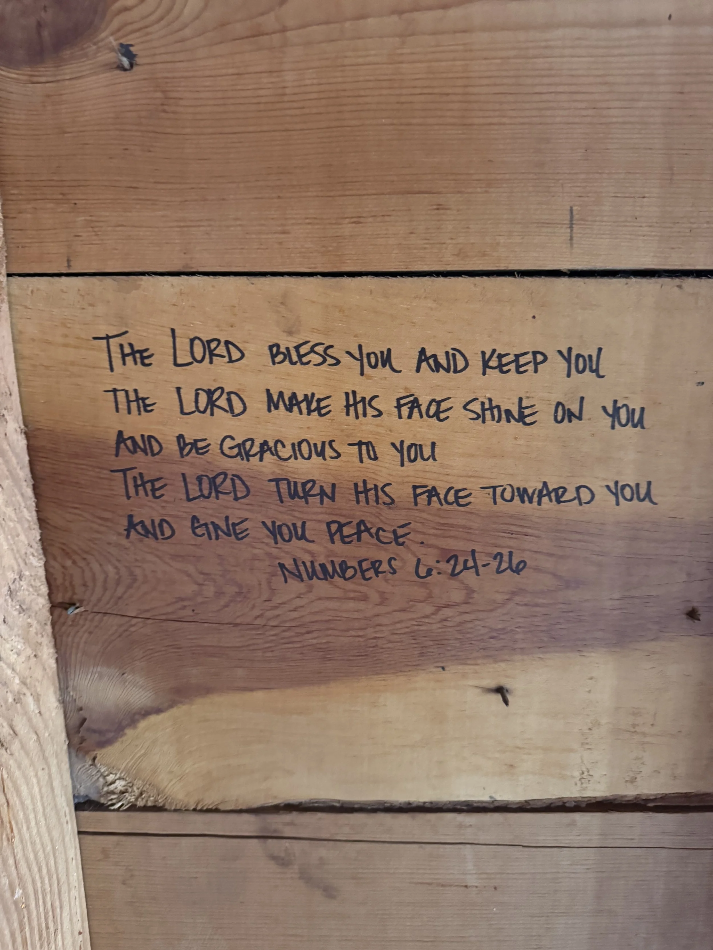 A handwritten Bible verse on a wooden wall that says, 'The Lord bless you and keep you. The Lord make his face shine on you and be gracious to you. The Lord turn his face toward you and give you peace. Numbers 6:24-26.'