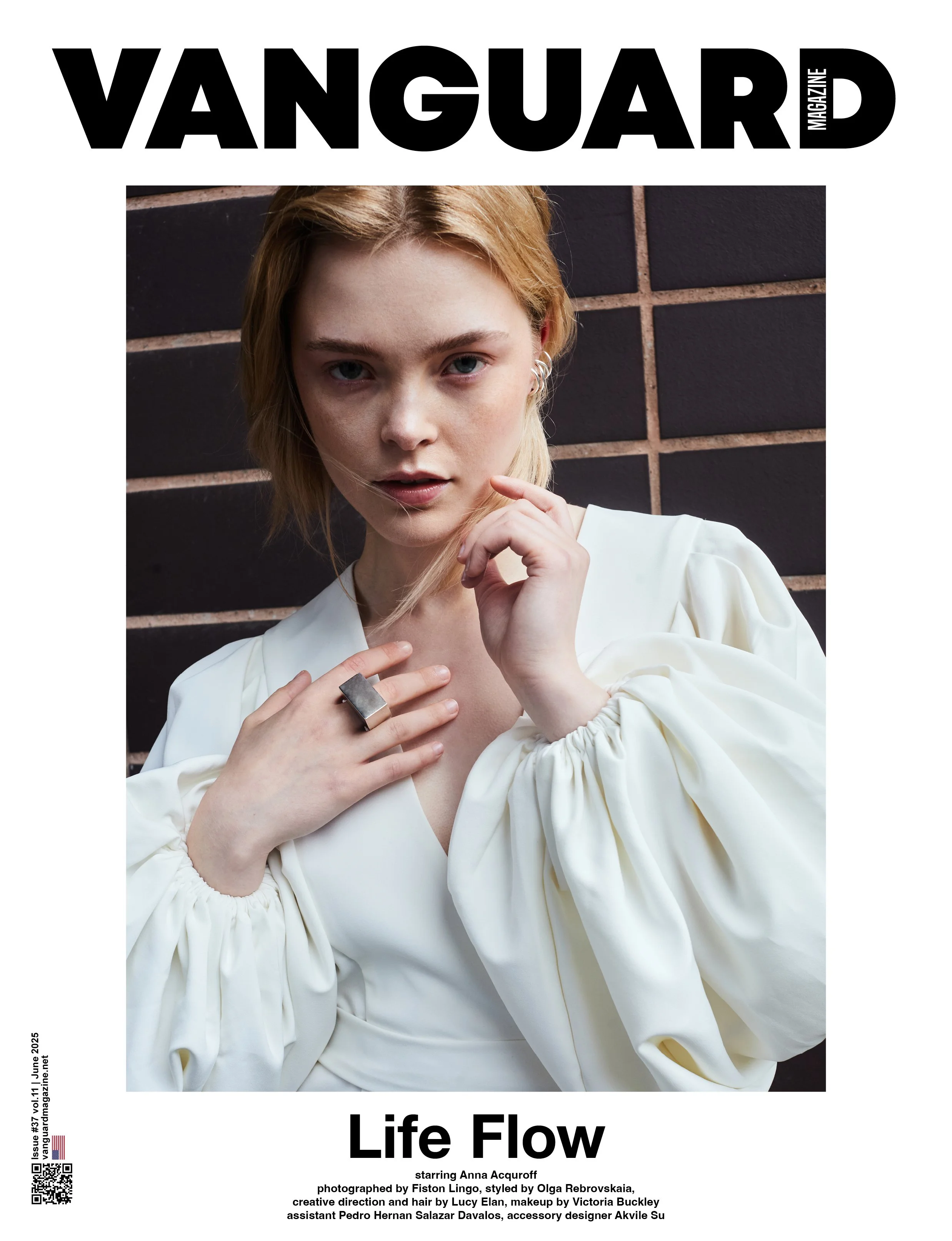 Cover of Vanguard magazine featuring a woman with blonde hair in a white designer blouse with puffed sleeves, posing against a dark brick wall.