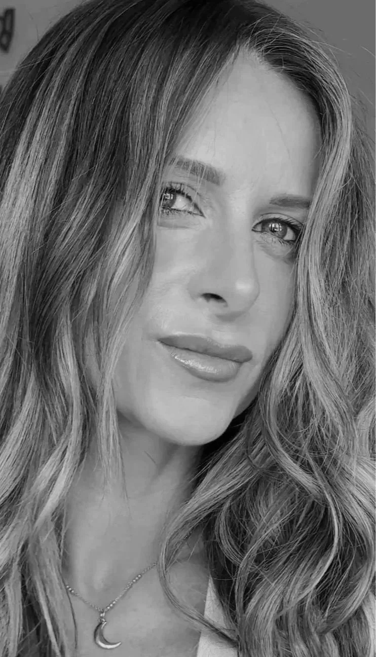 Close-up black and white photo of a woman with wavy hair, light-colored eyes, and a moon pendant necklace.