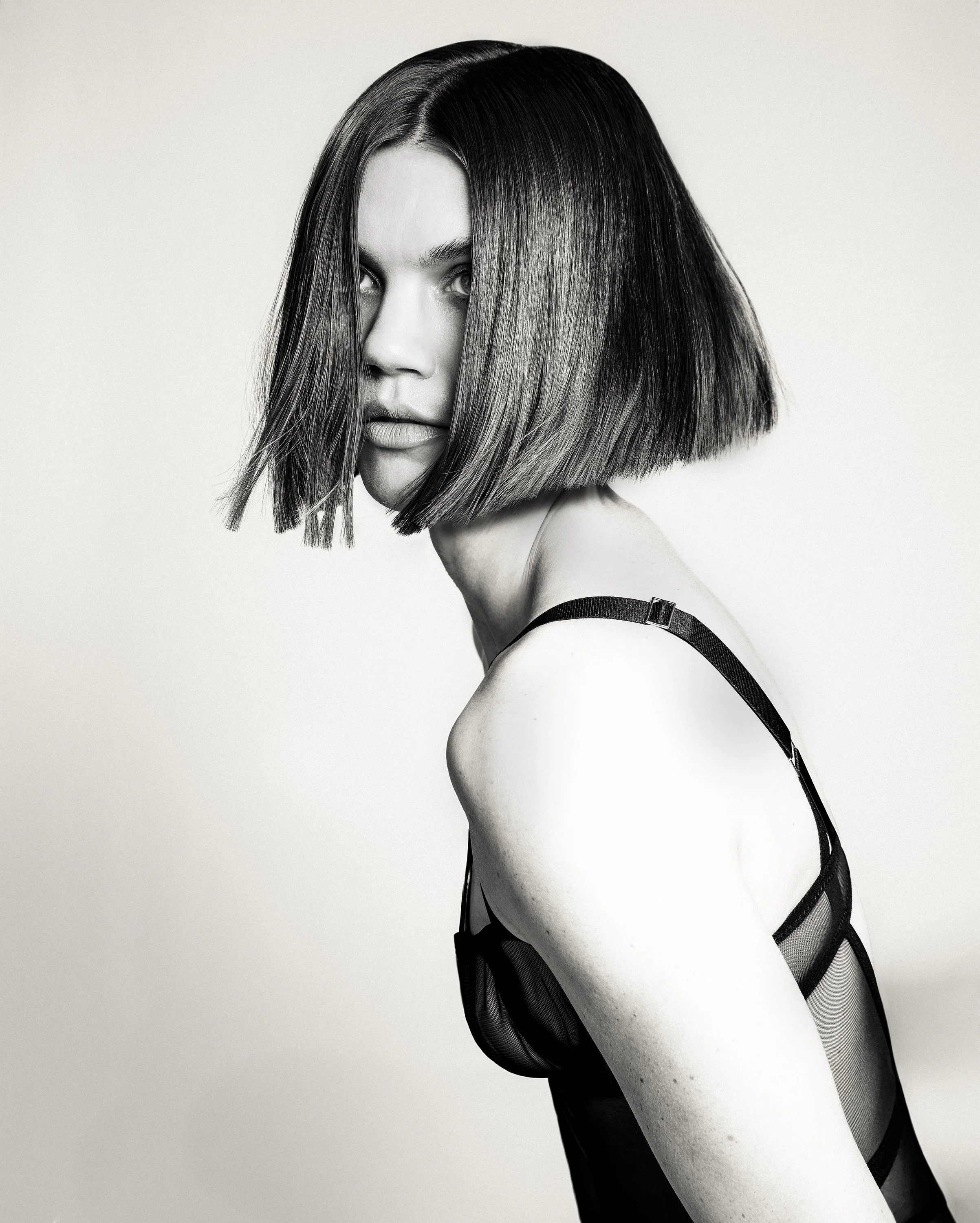 A woman with a short bob hairstyle and partially covering hair looking over her shoulder in black and white.