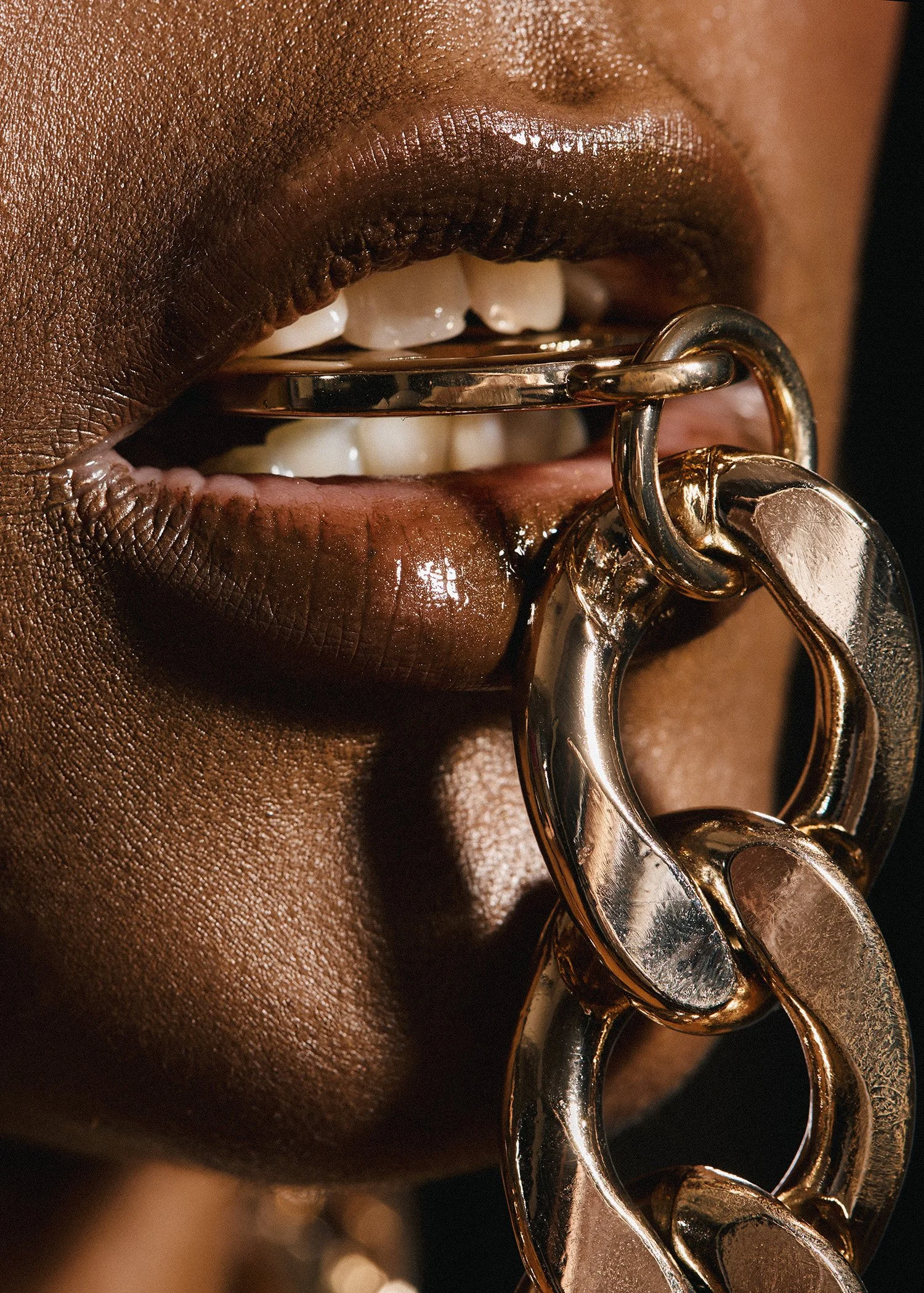 Close-up of a person's lips holding a gold chain in their mouth.