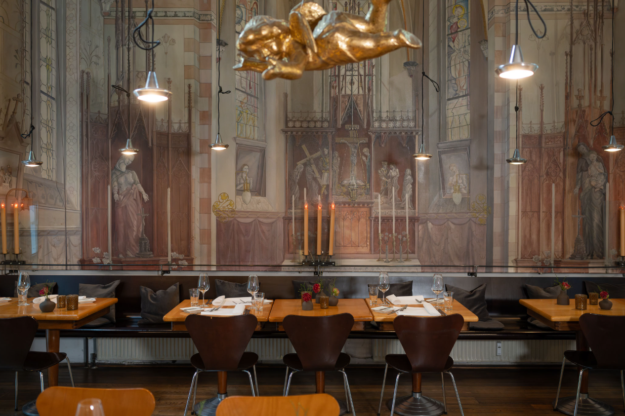 Elegantes Restaurantinterieur mit gemalter Wand im gotischen Stil, Holztischen, Stühlen, Tischgedecken und hängenden Lampen.