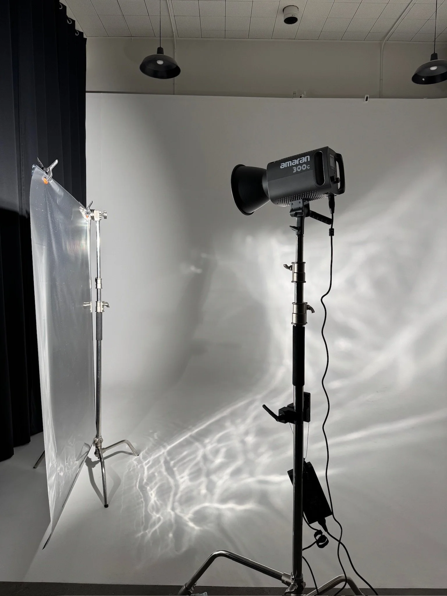 Photography studio setup with lighting equipment, a backdrop, and a stand on a white floor with a plain wall background.