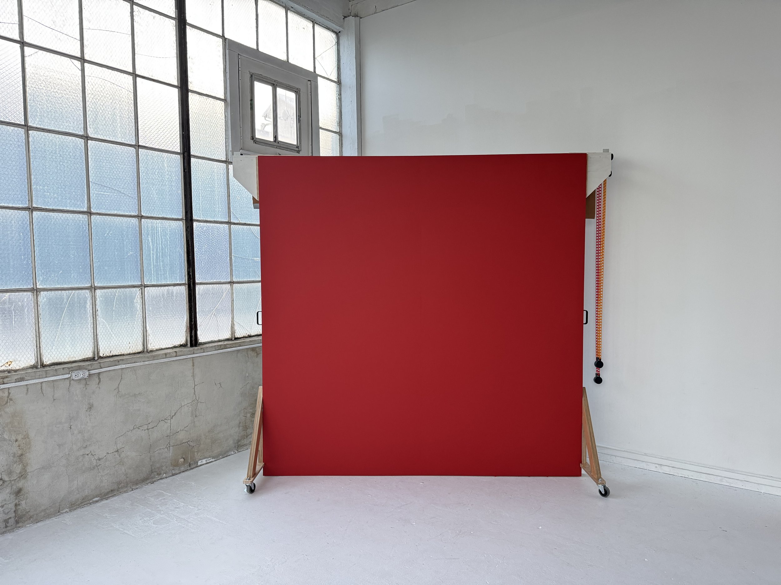 Red background with a white metal frame in a room with large industrial windows and white walls.