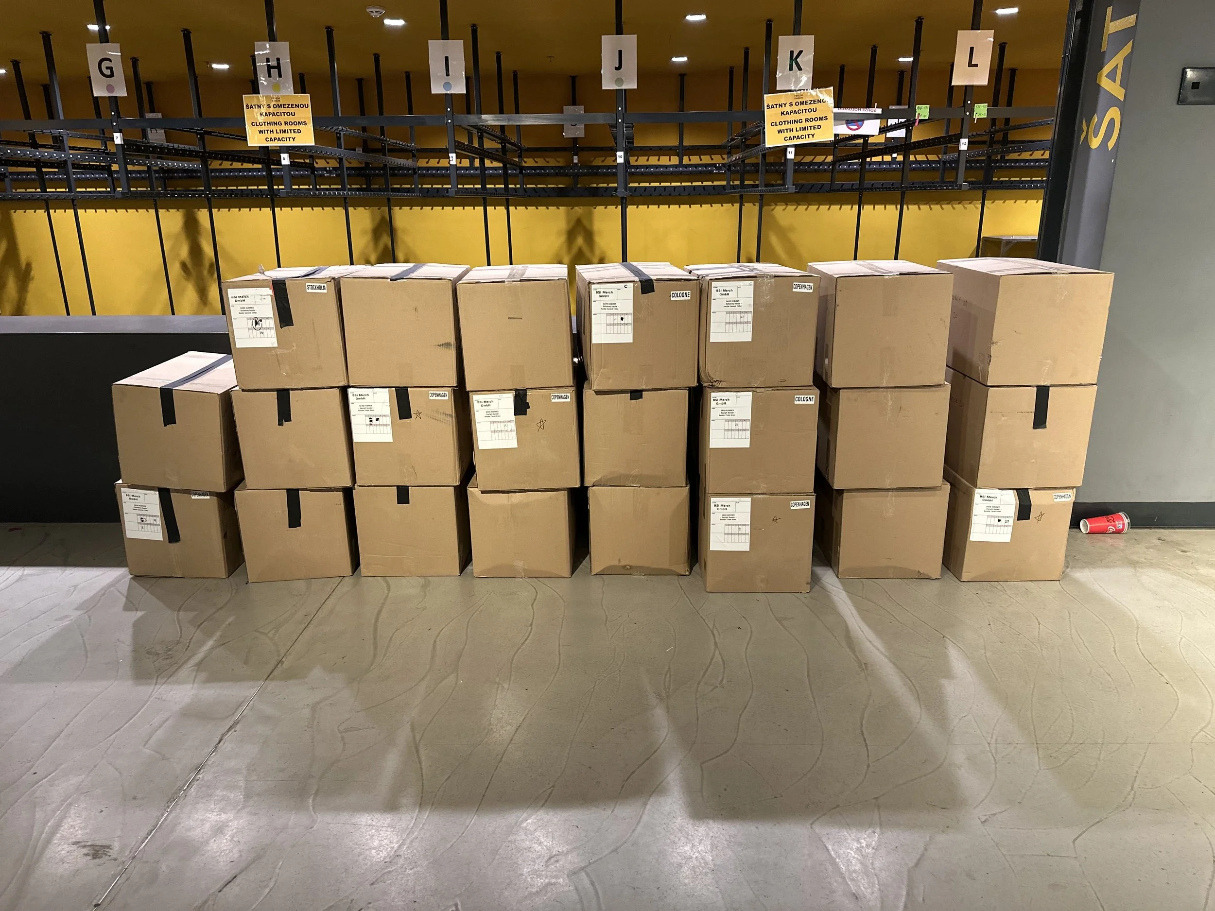 Neatly stacked cardboard boxes of touring merchandise in front of a stand.