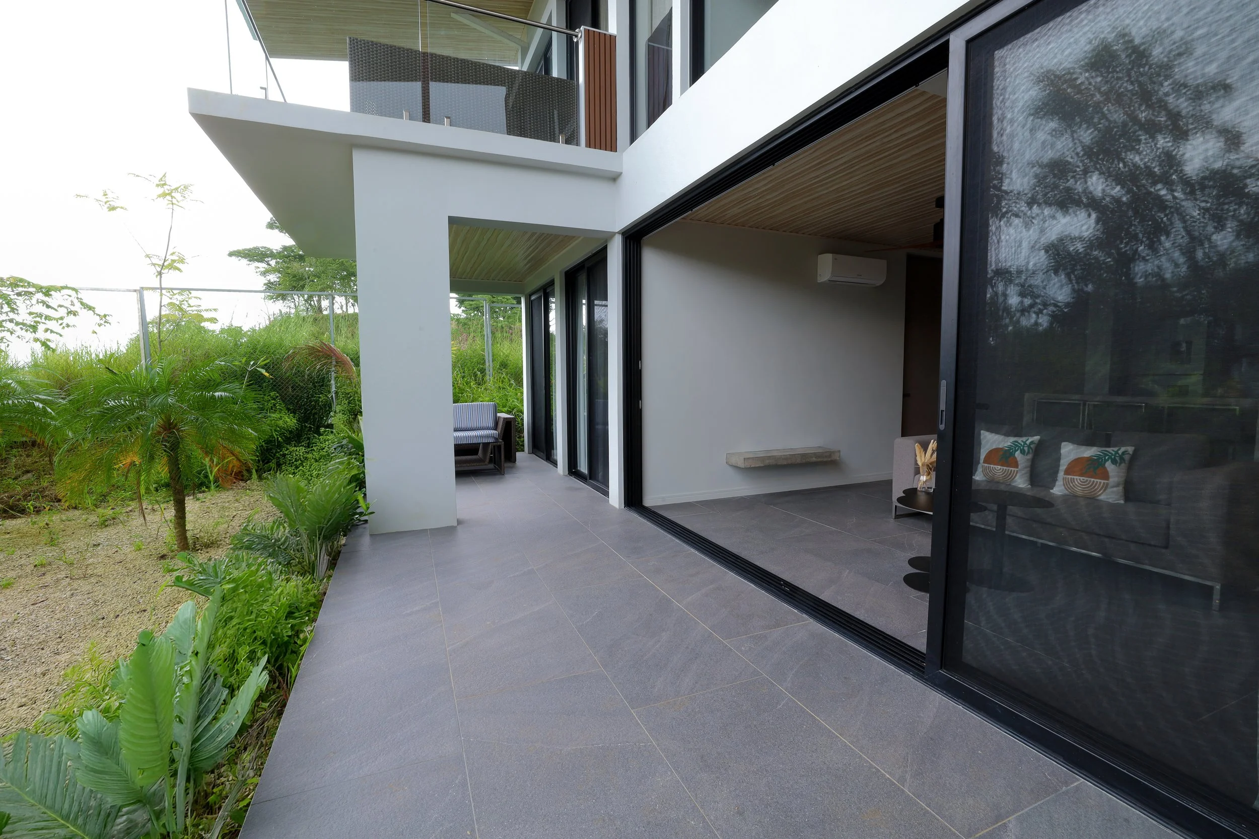 Private modern house patio with gray tile flooring and sliding glass doors, surrounded by lush greenery in Guanacaste.