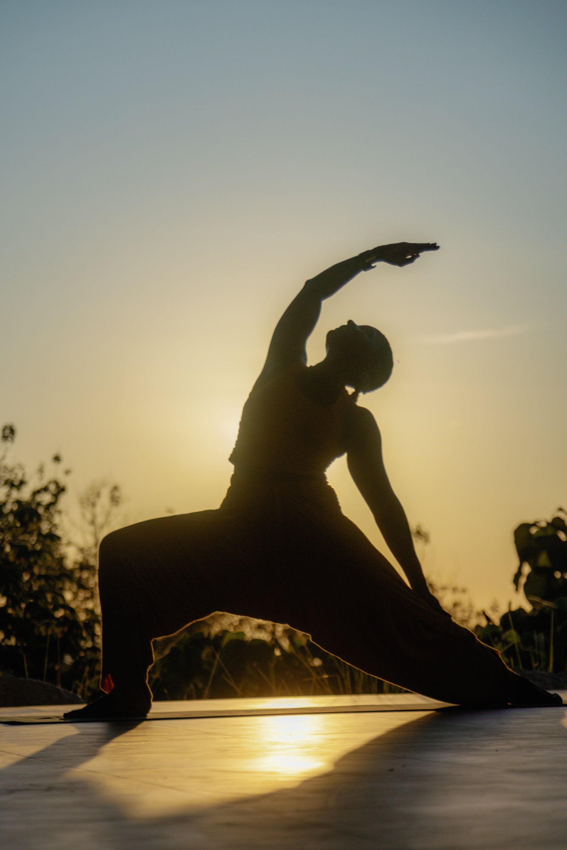 A person practicing yoga outdoors at sunset, in a lunge pose with one arm reaching overhead.