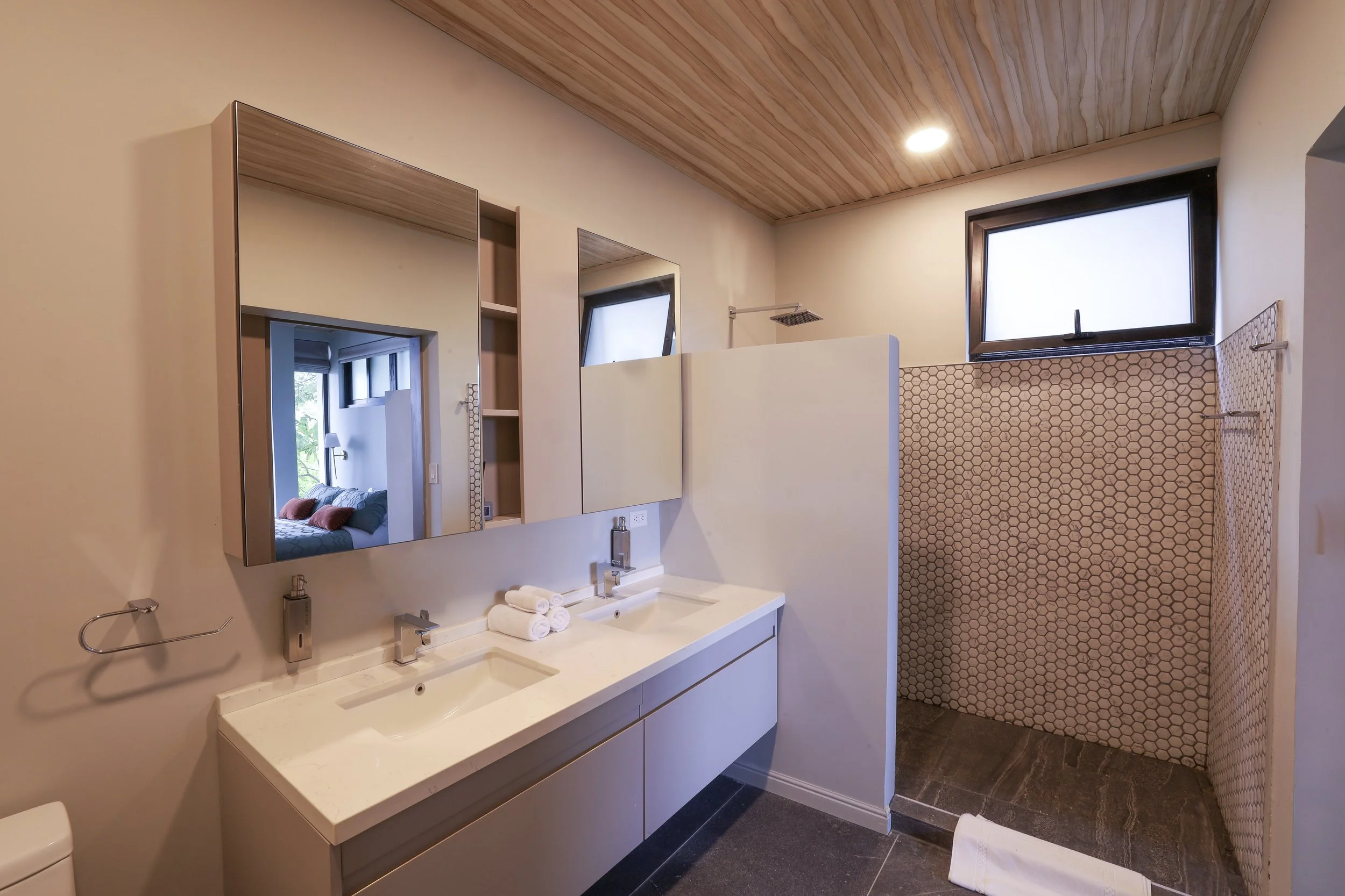 Contemporary bathroom with double sinks, large mirror, and a walk-in shower with stylish hexagonal tile walls.